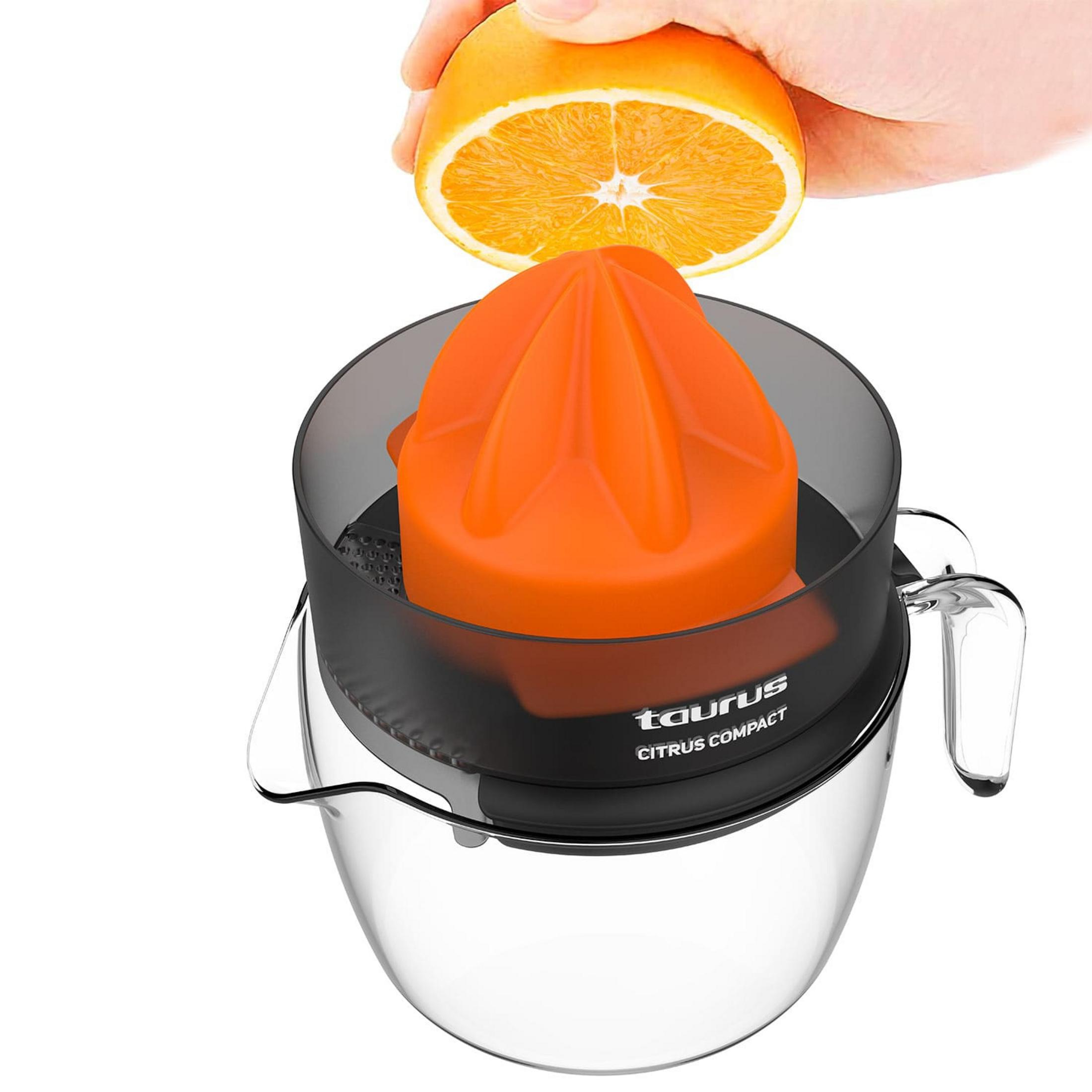 Una mano presiona media naranja sobre un exprimidor naranja con base de cristal.
