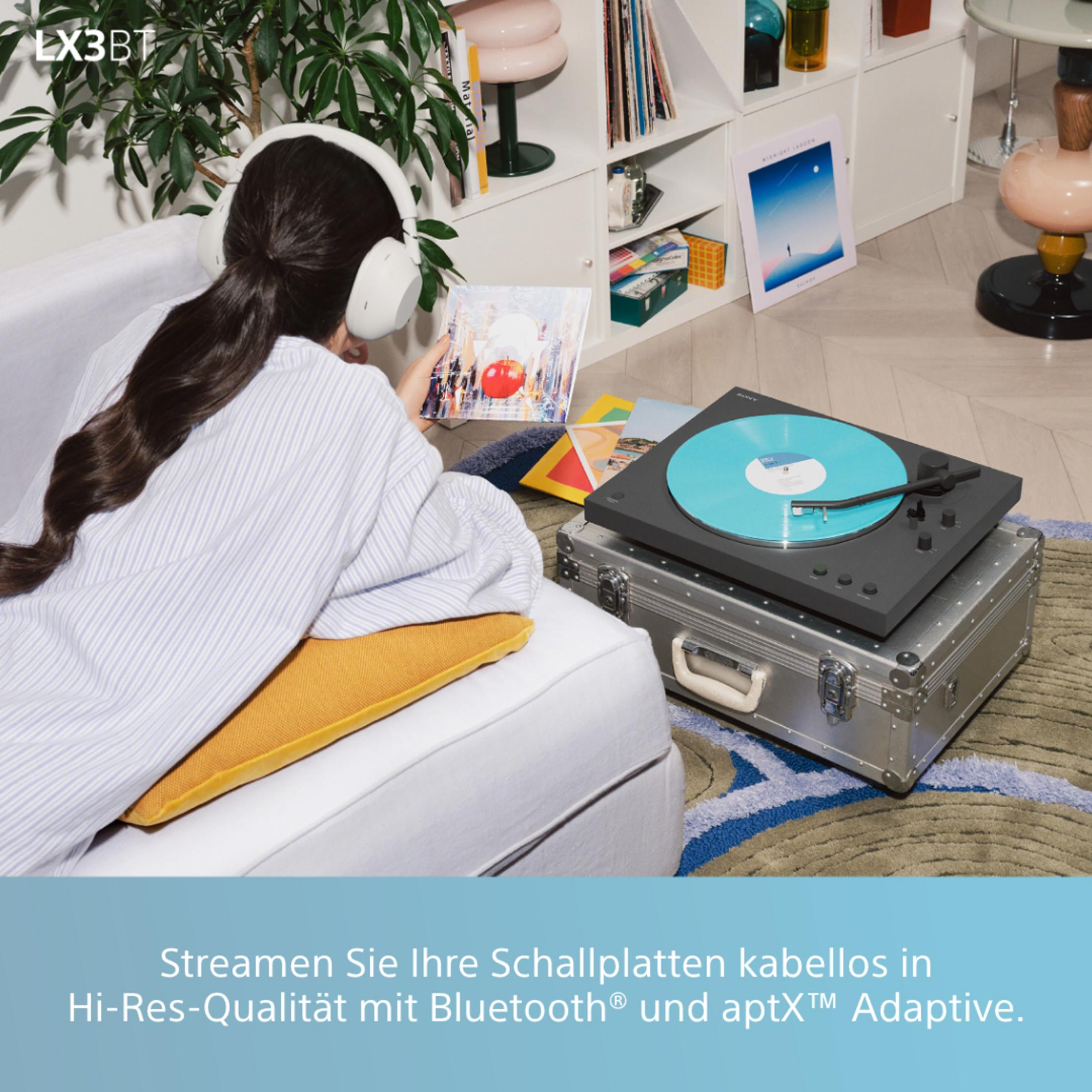 Donna con cuffie tiene un disco accanto a un giradischi su una valigia.