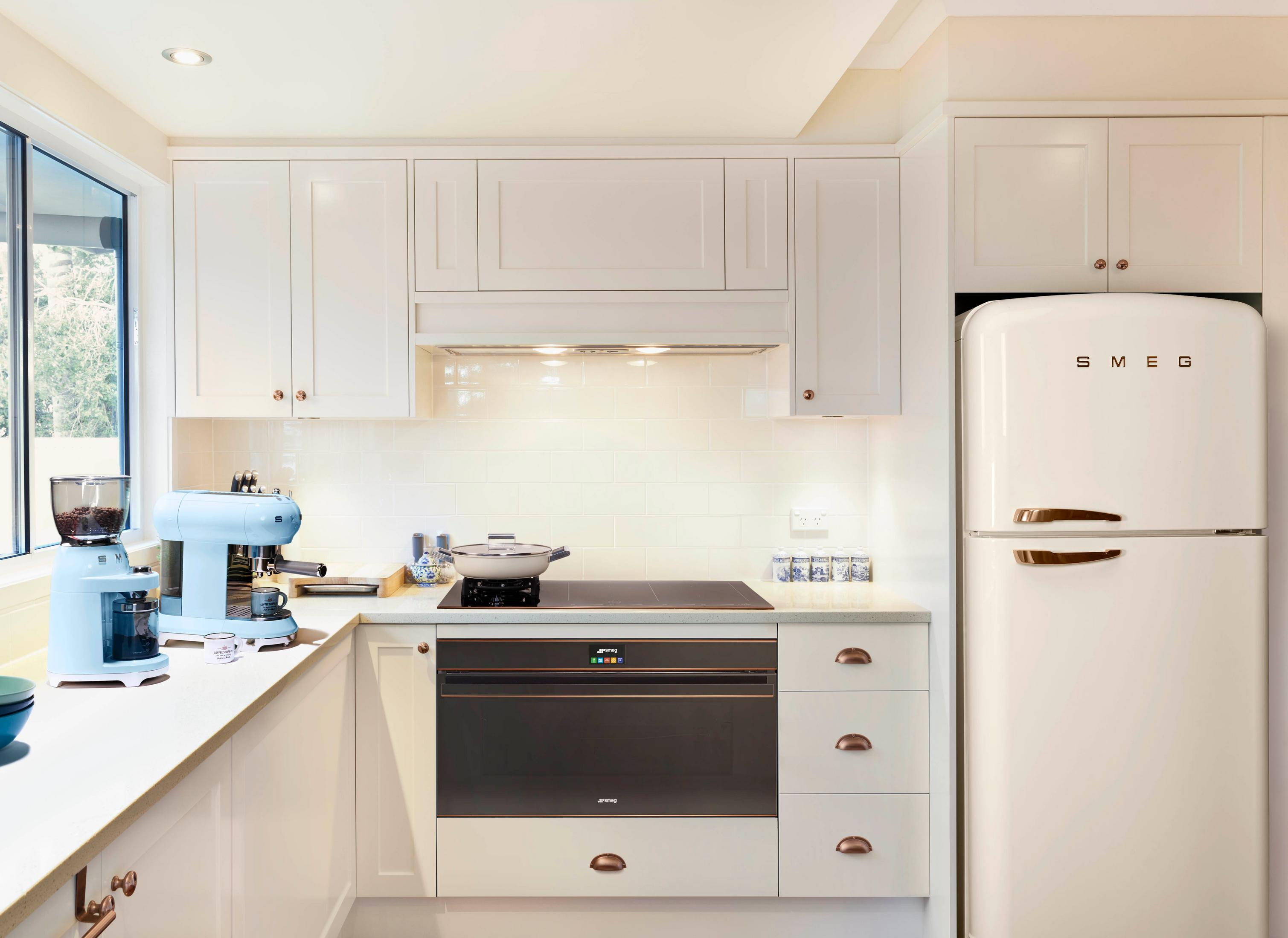 Una cocina blanca con cafetera, horno y refrigerador azules.