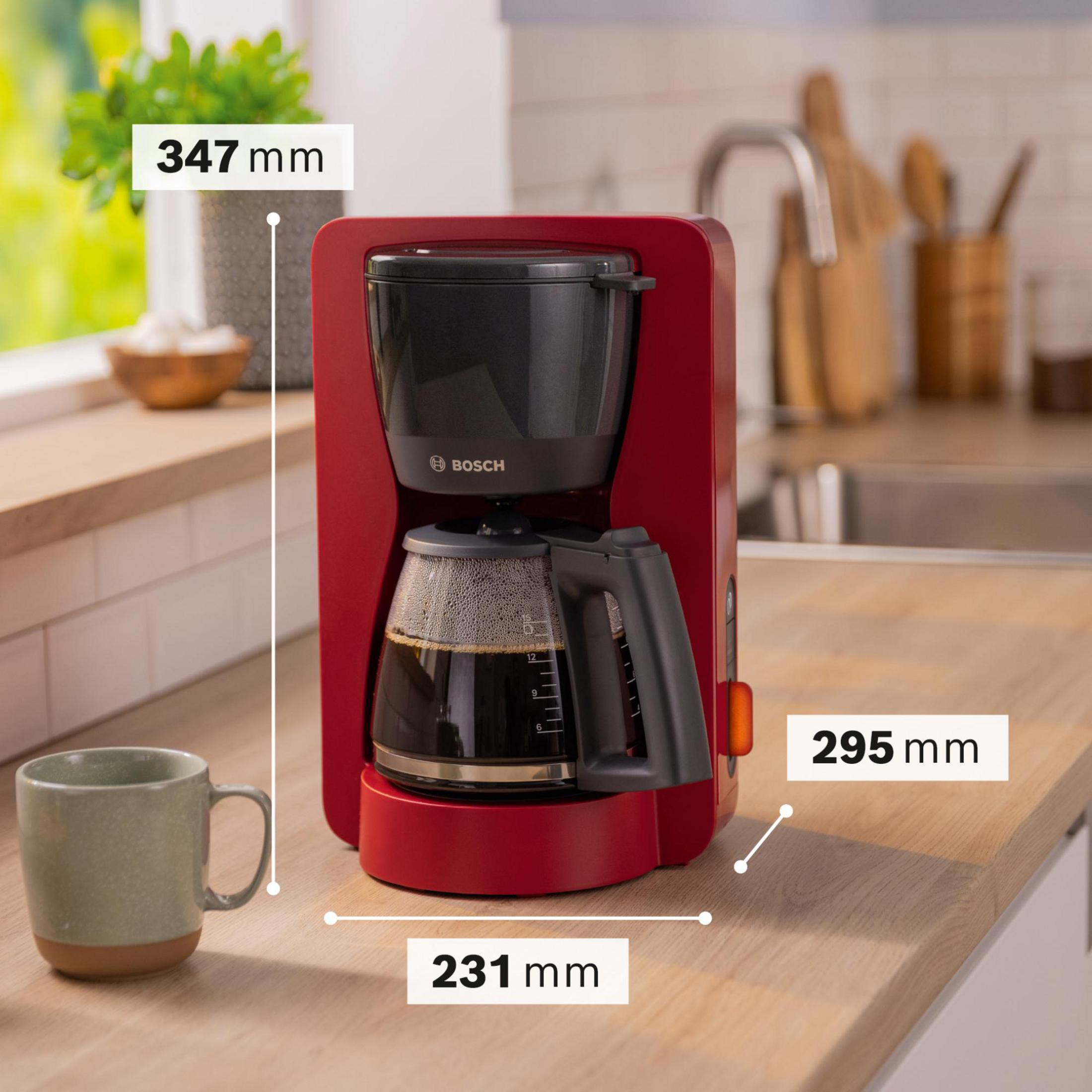 Una cafetera roja con jarra de cristal está sobre una superficie de madera junto a una taza.