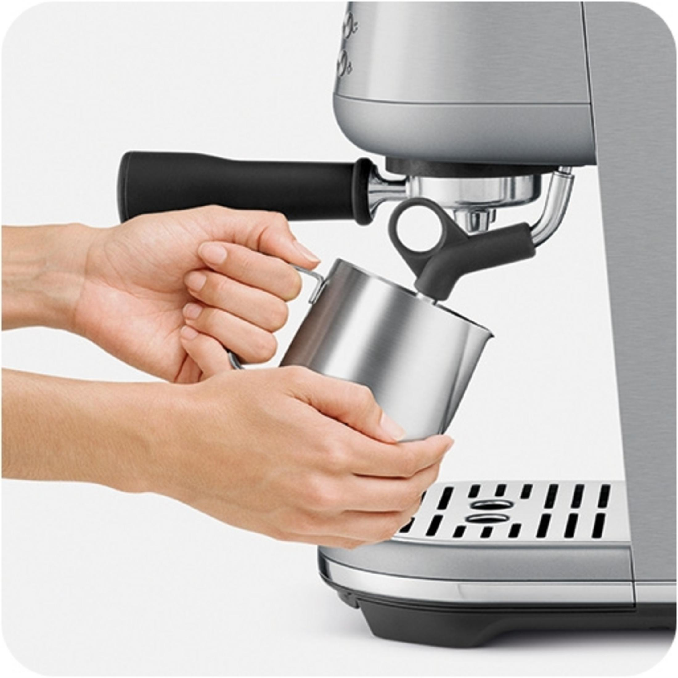 Hände halten einen Metallmilchkrug unter die Dampfdüse einer Espressomaschine.