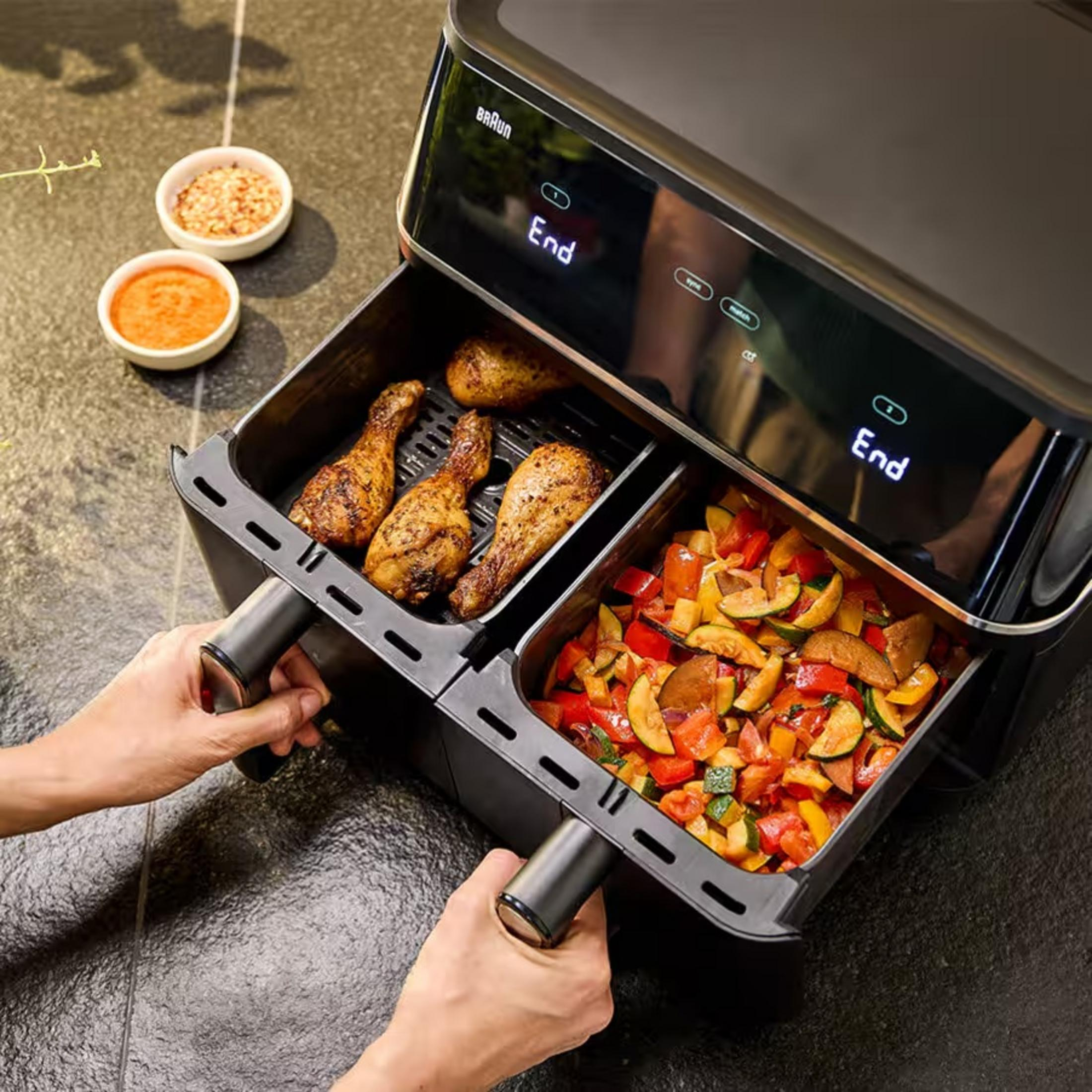 Doppia friggitrice ad aria con cosce di pollo e verdure. Mani che estraggono i cassetti.