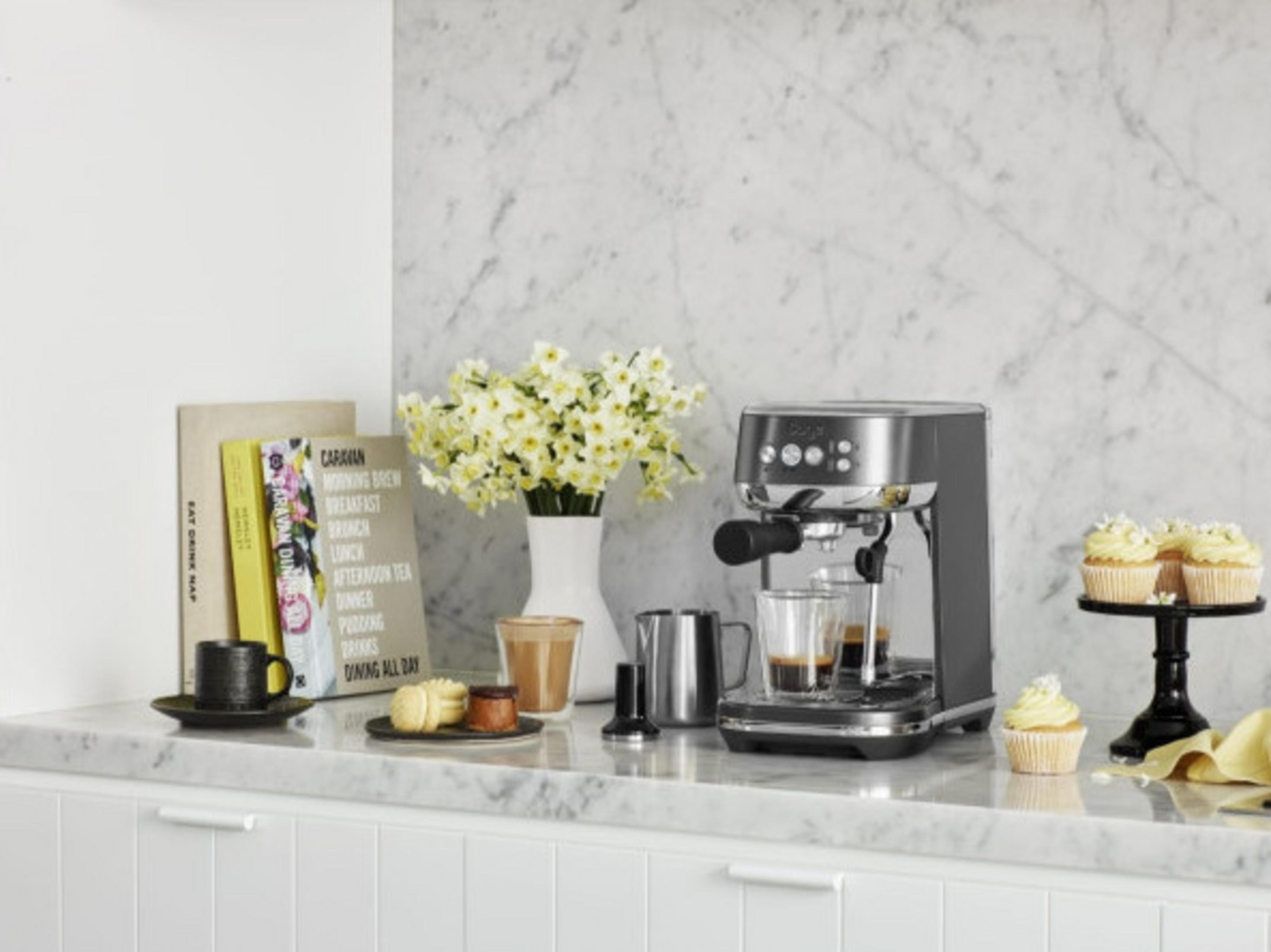 Machine à expresso avec tasses, petits gâteaux et fleurs sur un plan de travail en marbre.