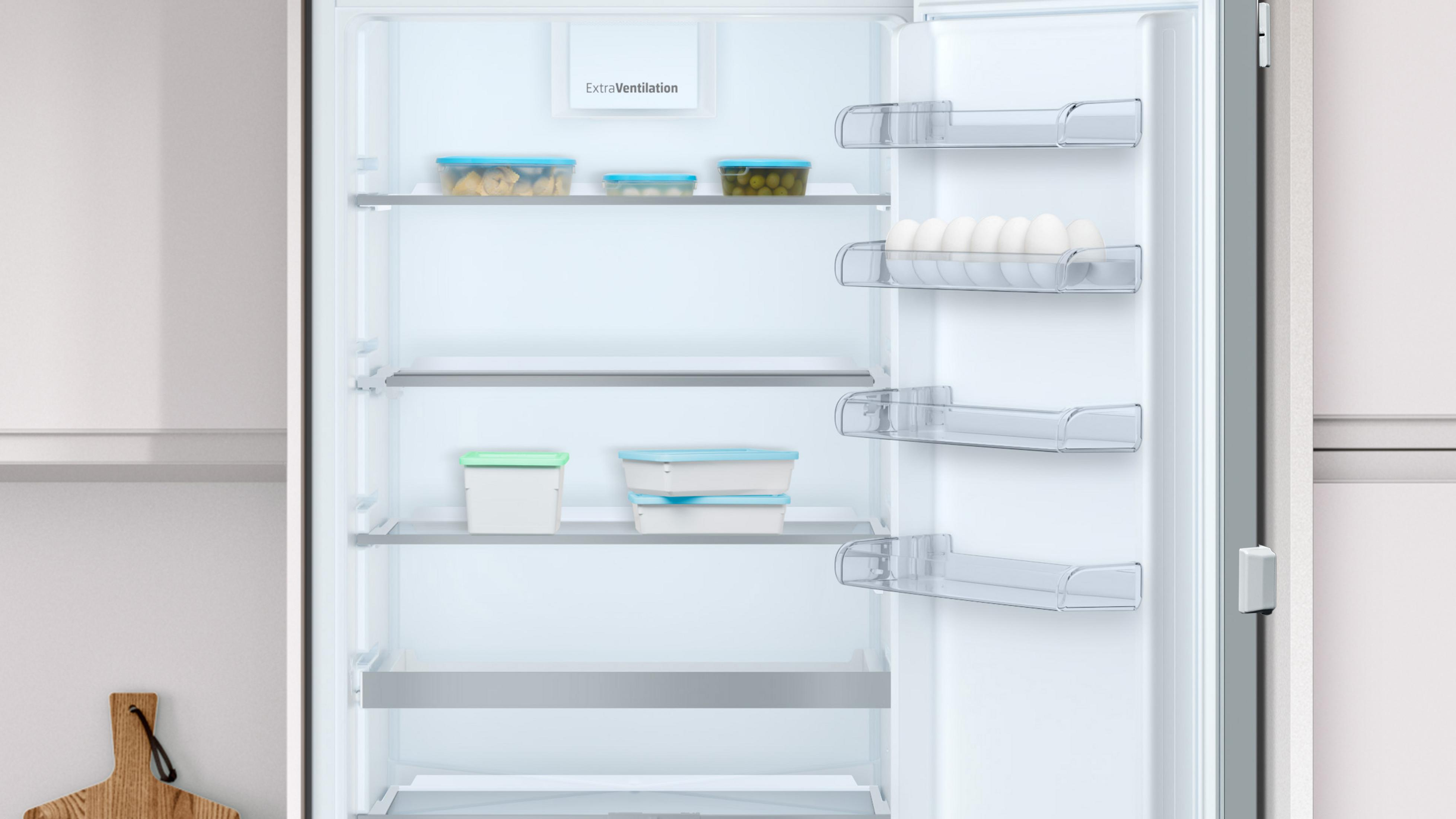 Un refrigerador abierto con huevos, recipientes y aceitunas dentro.