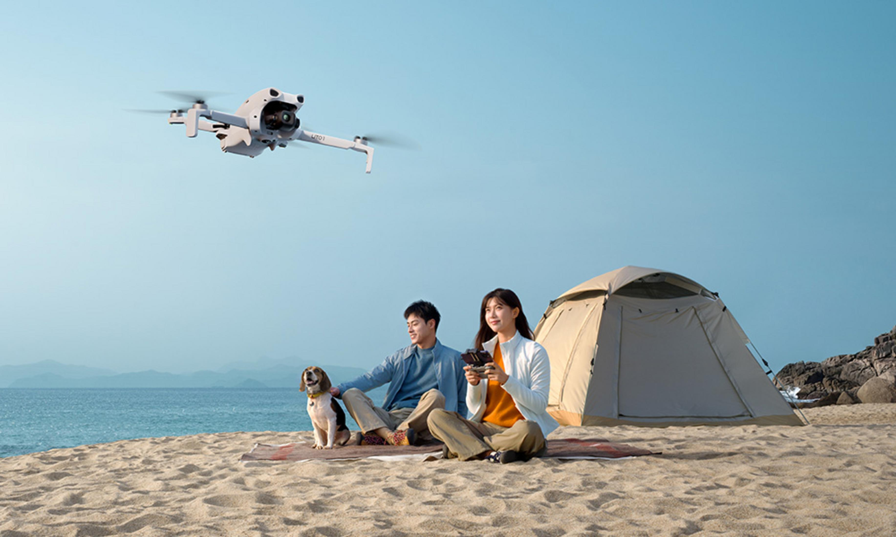 Un hombre, una mujer y un perro se sientan en la playa mientras un dron vuela.