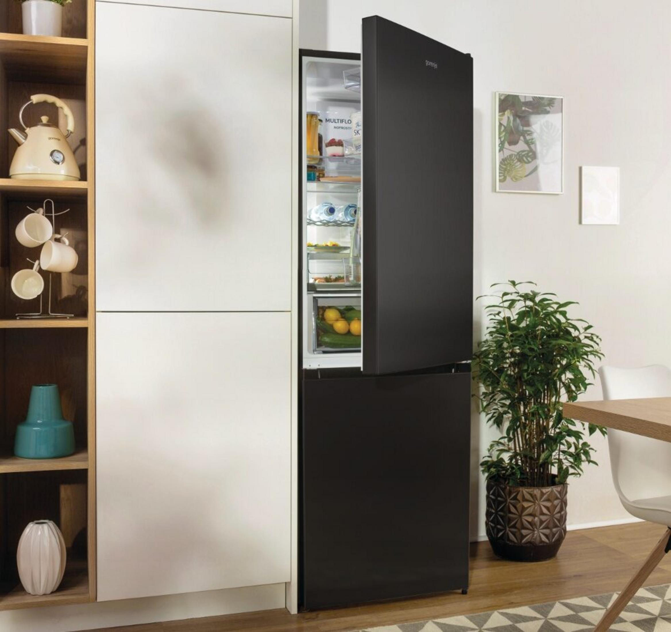 Un frigorifero nero con la porta aperta, vicino a mobili bianchi. All'interno sono visibili alimenti.