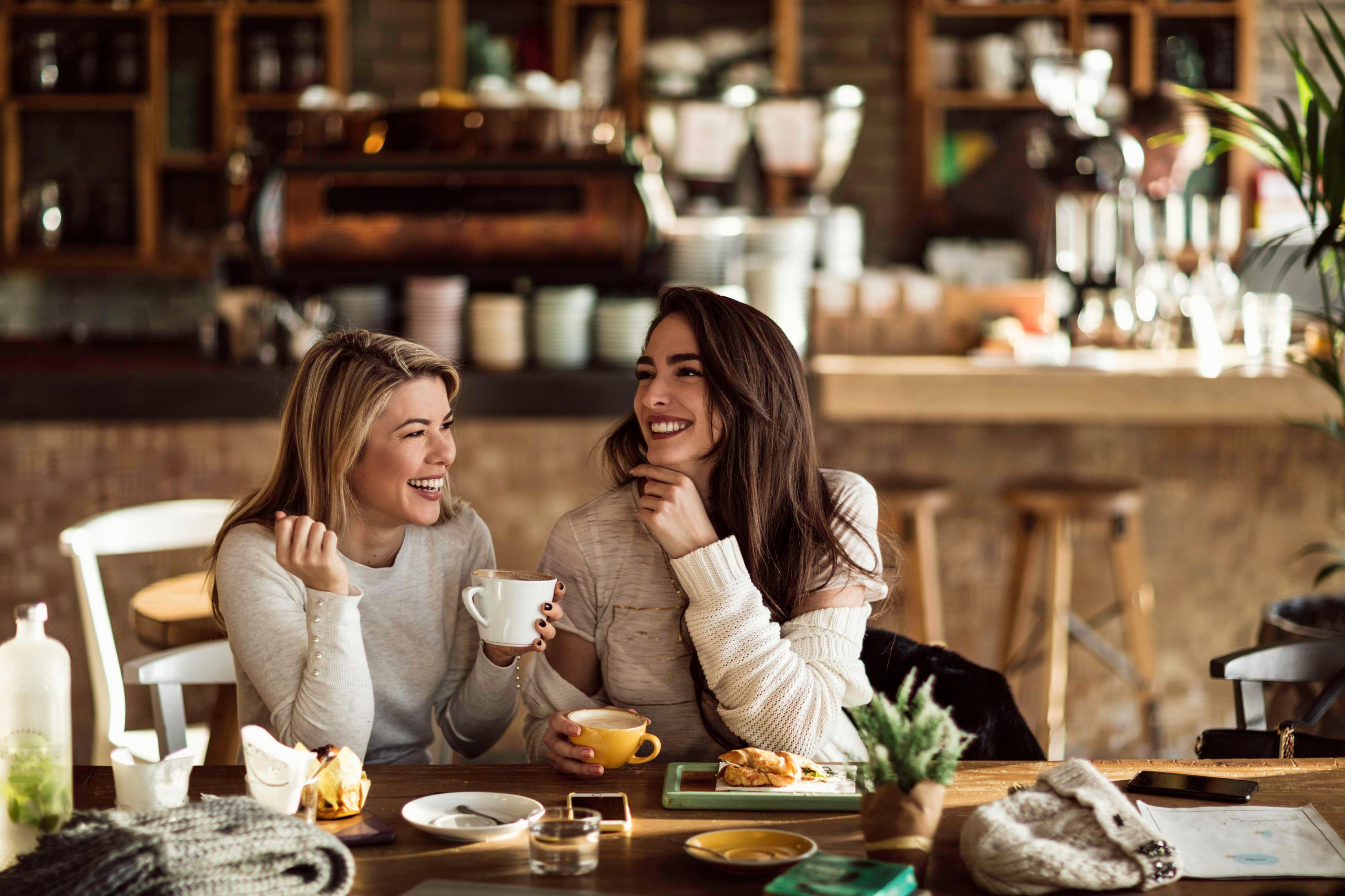 Due donne ridono bevendo caffè a un tavolo da bar.