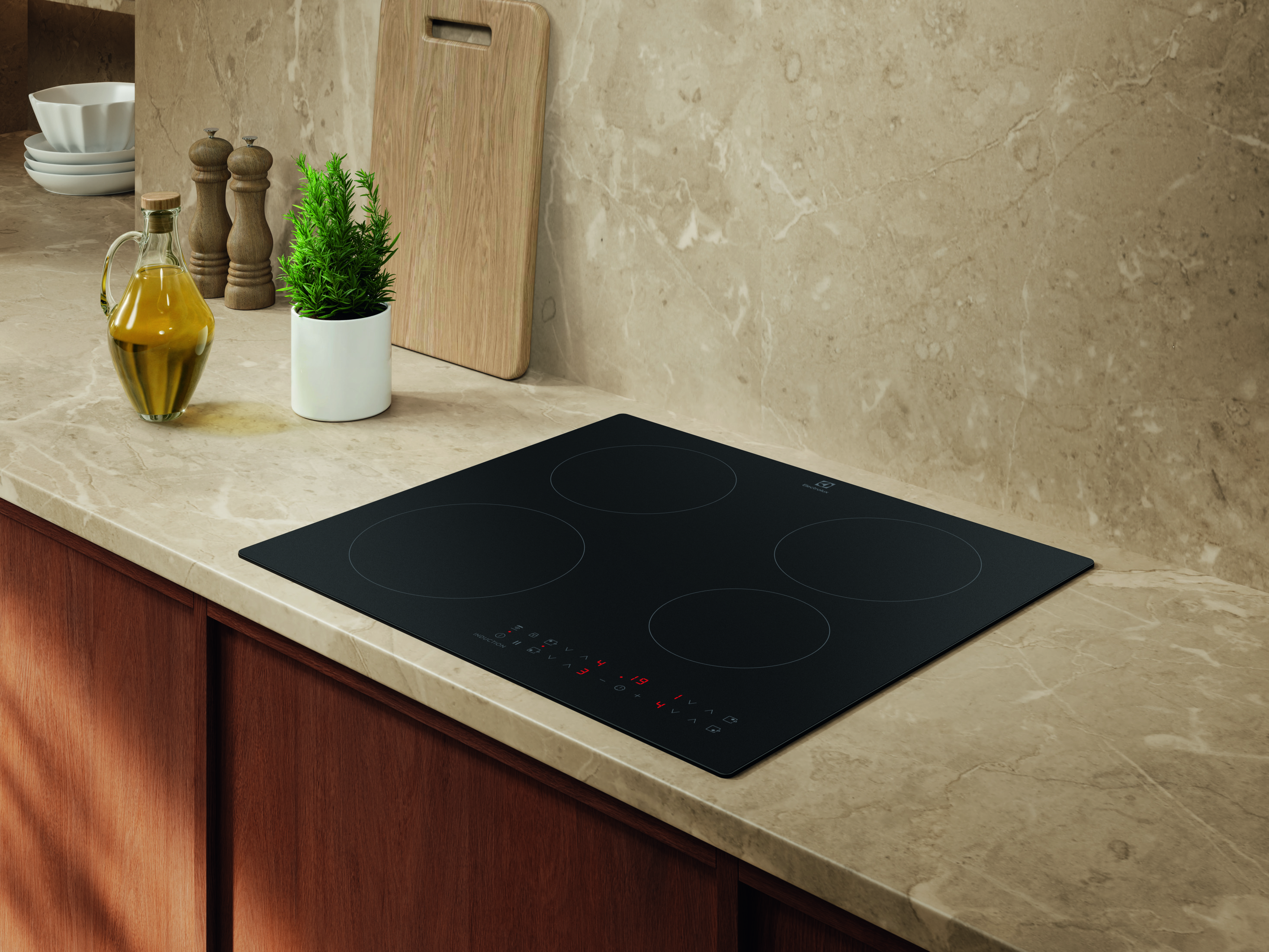 Un piano cottura a induzione nero con quattro zone di cottura su un piano di lavoro in marmo beige.