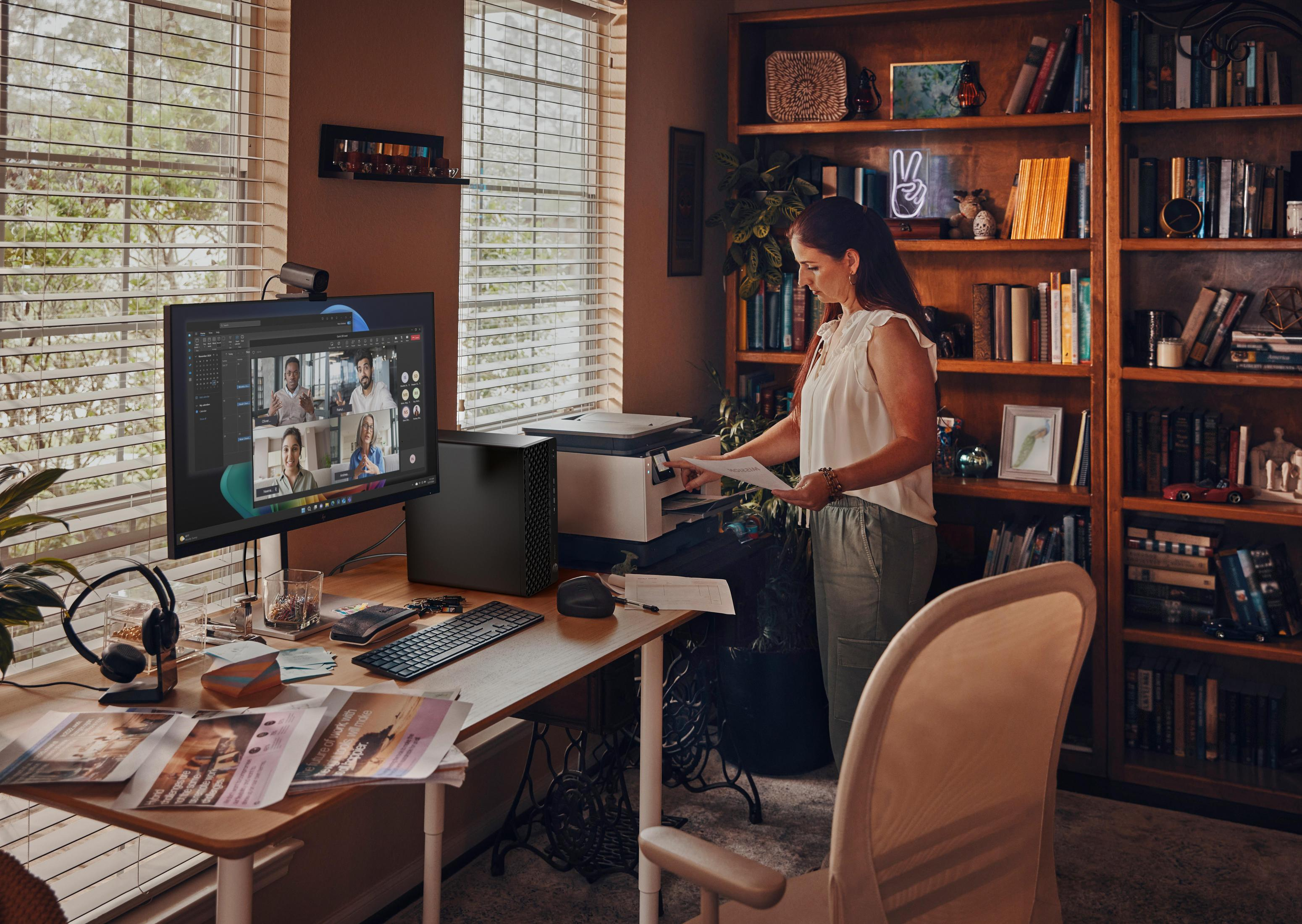 Femme à un bureau avec ordinateur, imprimante et bibliothèque. Appel vidéo à l'écran.