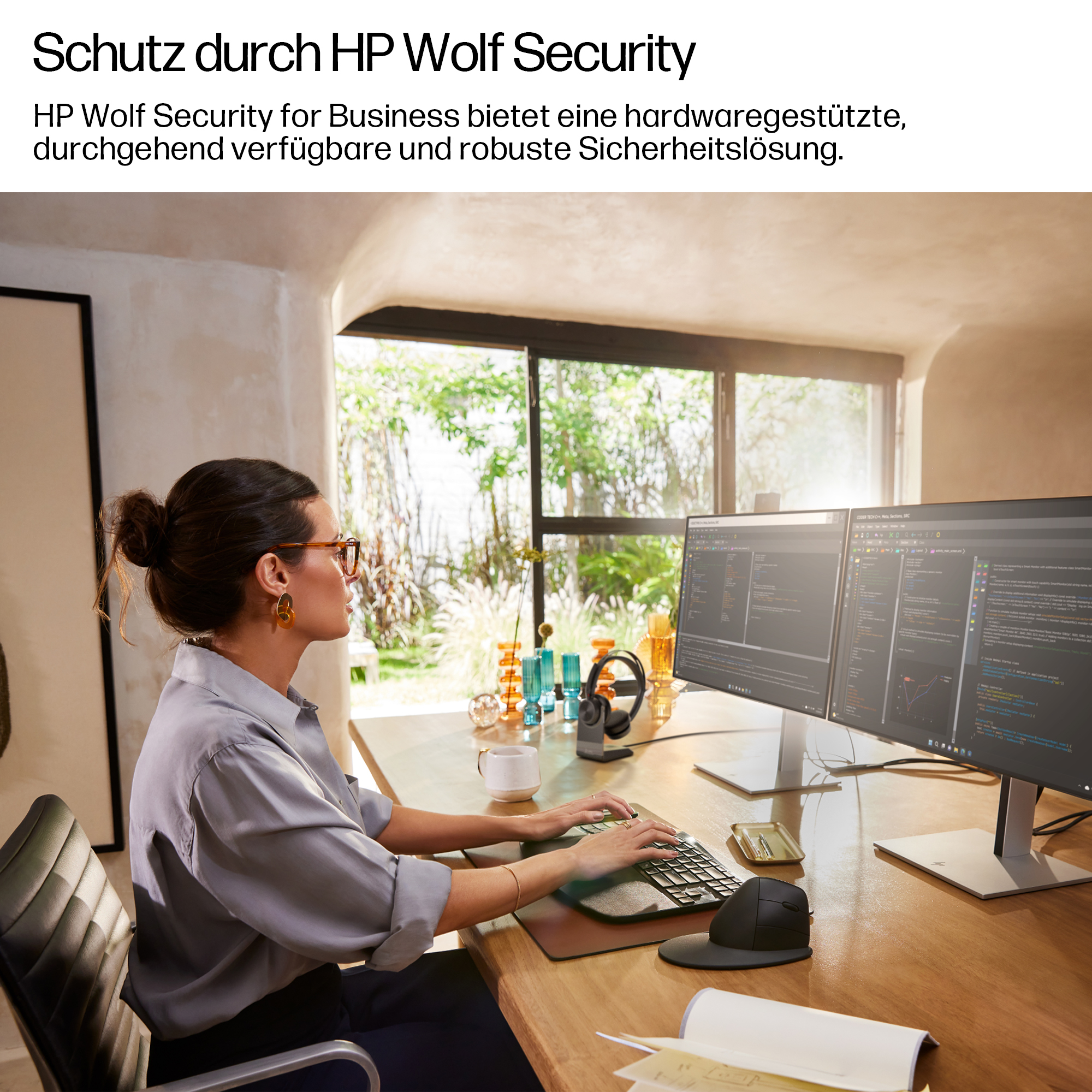 Eine Frau mit Brille arbeitet an zwei Computermonitoren in einem hellen Büro.