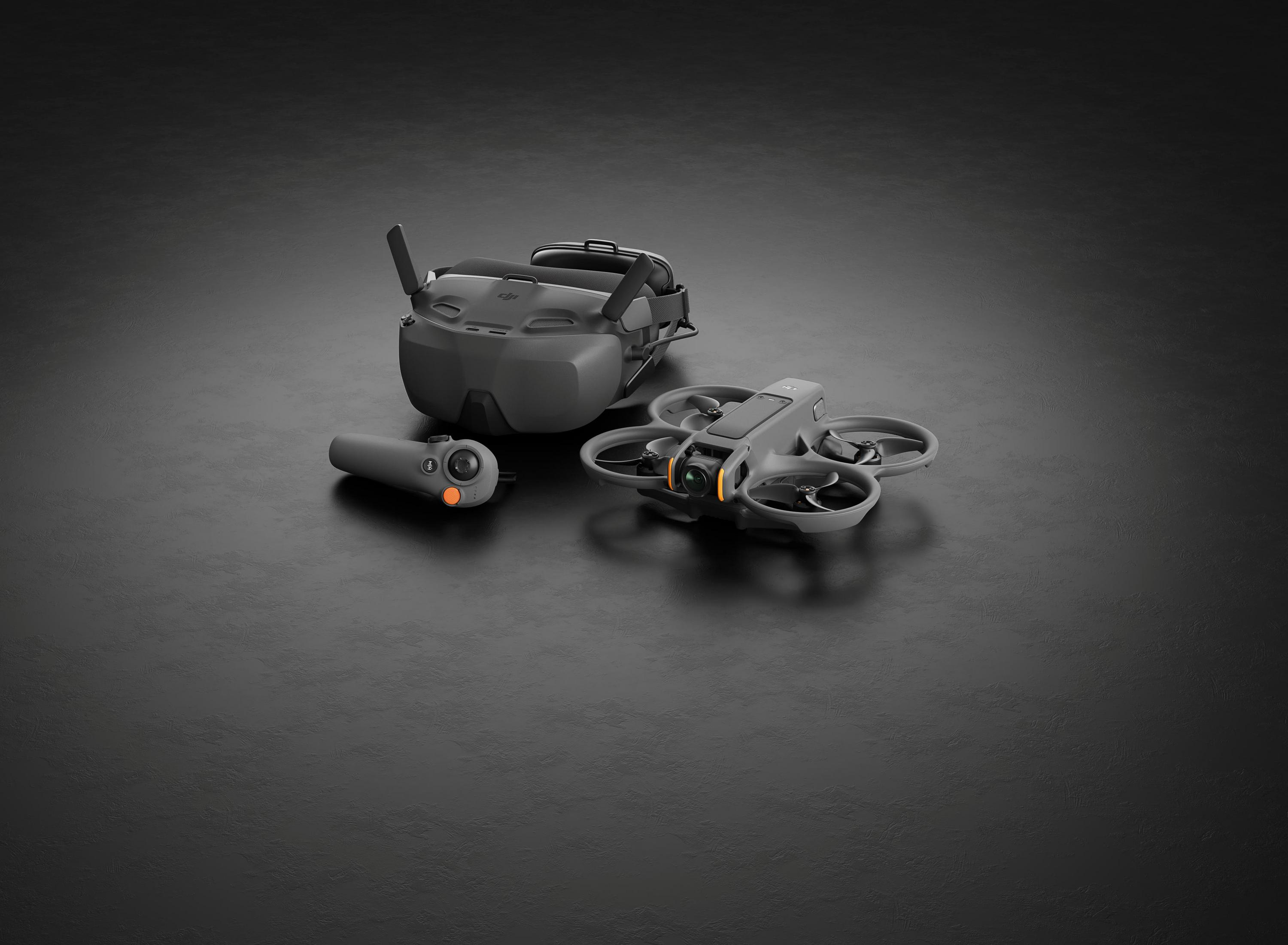 Occhiali FPV grigi, drone e controller su superficie scura e testurizzata.