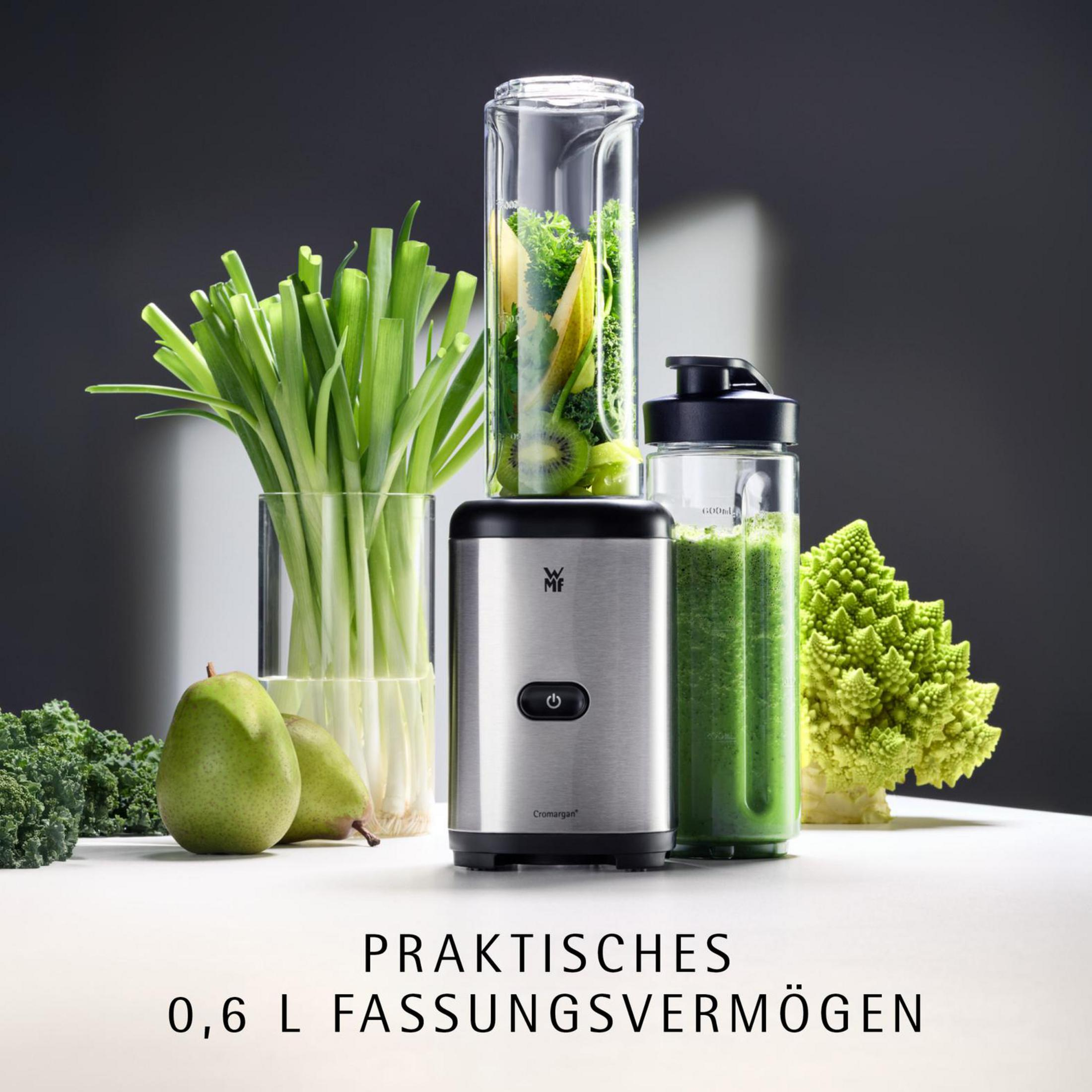 Gümüş rengi blender, yeşil malzemeler ve sebzeler masada.