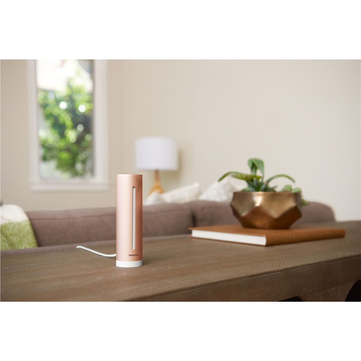 A copper cylinder stands on a wooden table. A sofa is in the background.