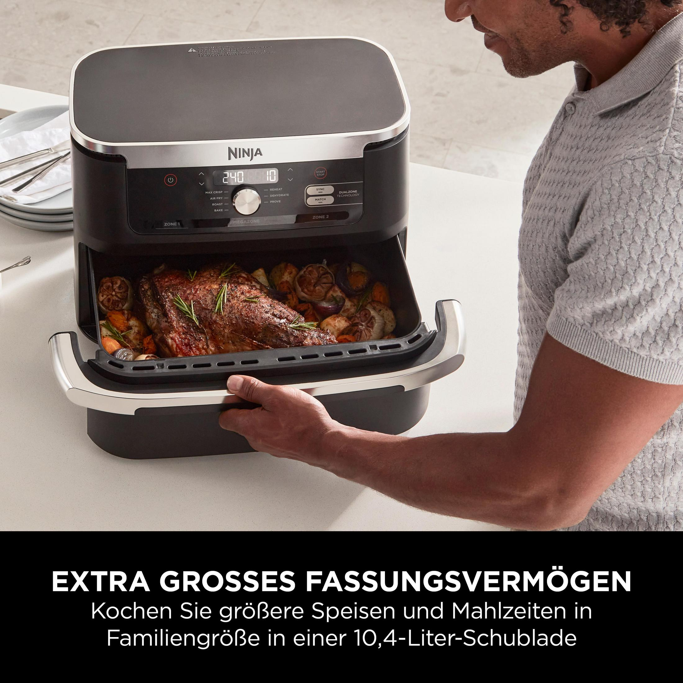 Un homme sort un tiroir Ninja Air Fryer avec de la viande rôtie et des légumes à l'intérieur.