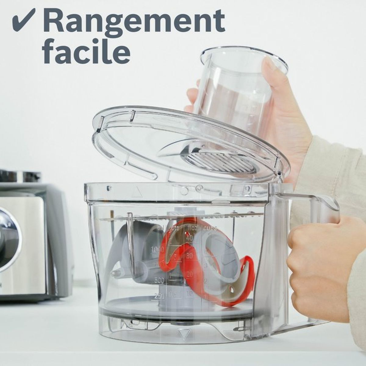 A hand places a clear measuring cup into a food processor bowl.