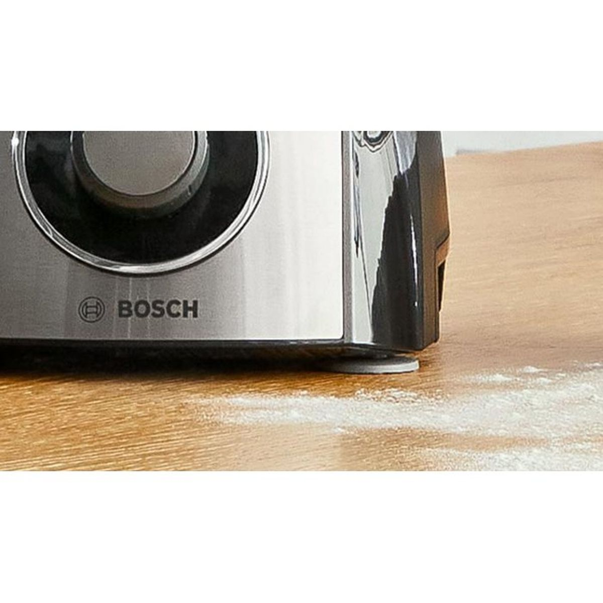 A silver Bosch mixer sits on a wooden table with some flour beside it.