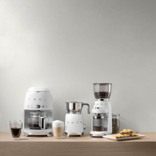 Weiße Smeg Kaffee-Geräte: Filterkaffeemaschine, Milchaufschäumer, Mühle, Kaffee, Latte und Kekse.