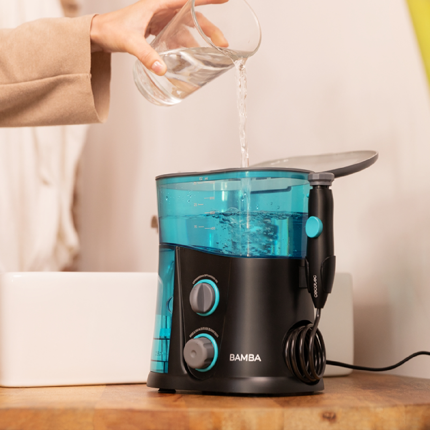 Una mano vierte agua de un vaso en un depósito negro de irrigador bucal.