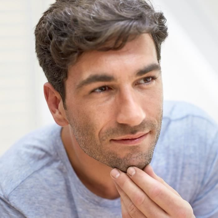Hombre con cabello castaño se toca la barbilla, viste camiseta azul.