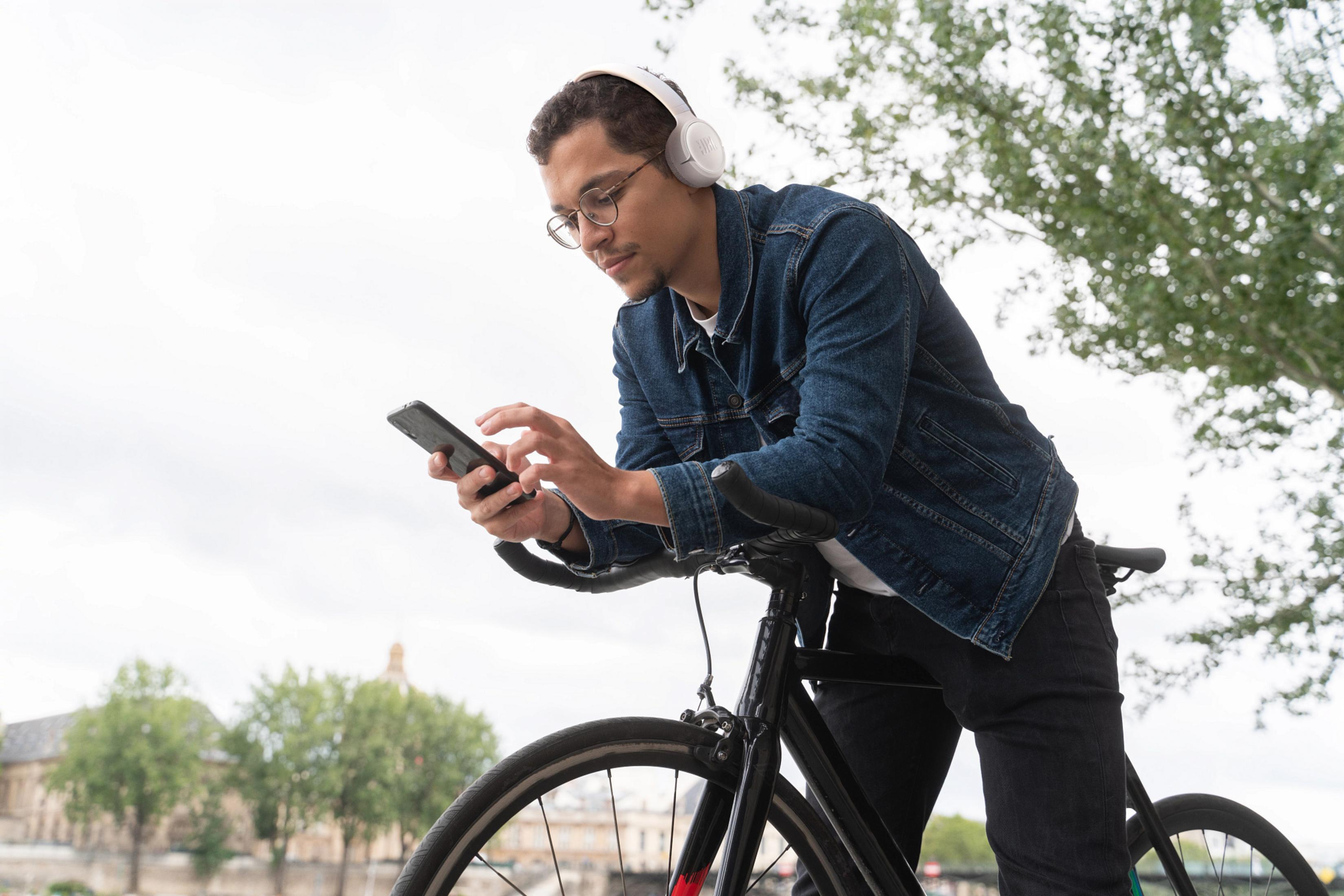 Uomo con cuffie e occhiali appoggiato a una bici usa il suo telefono.