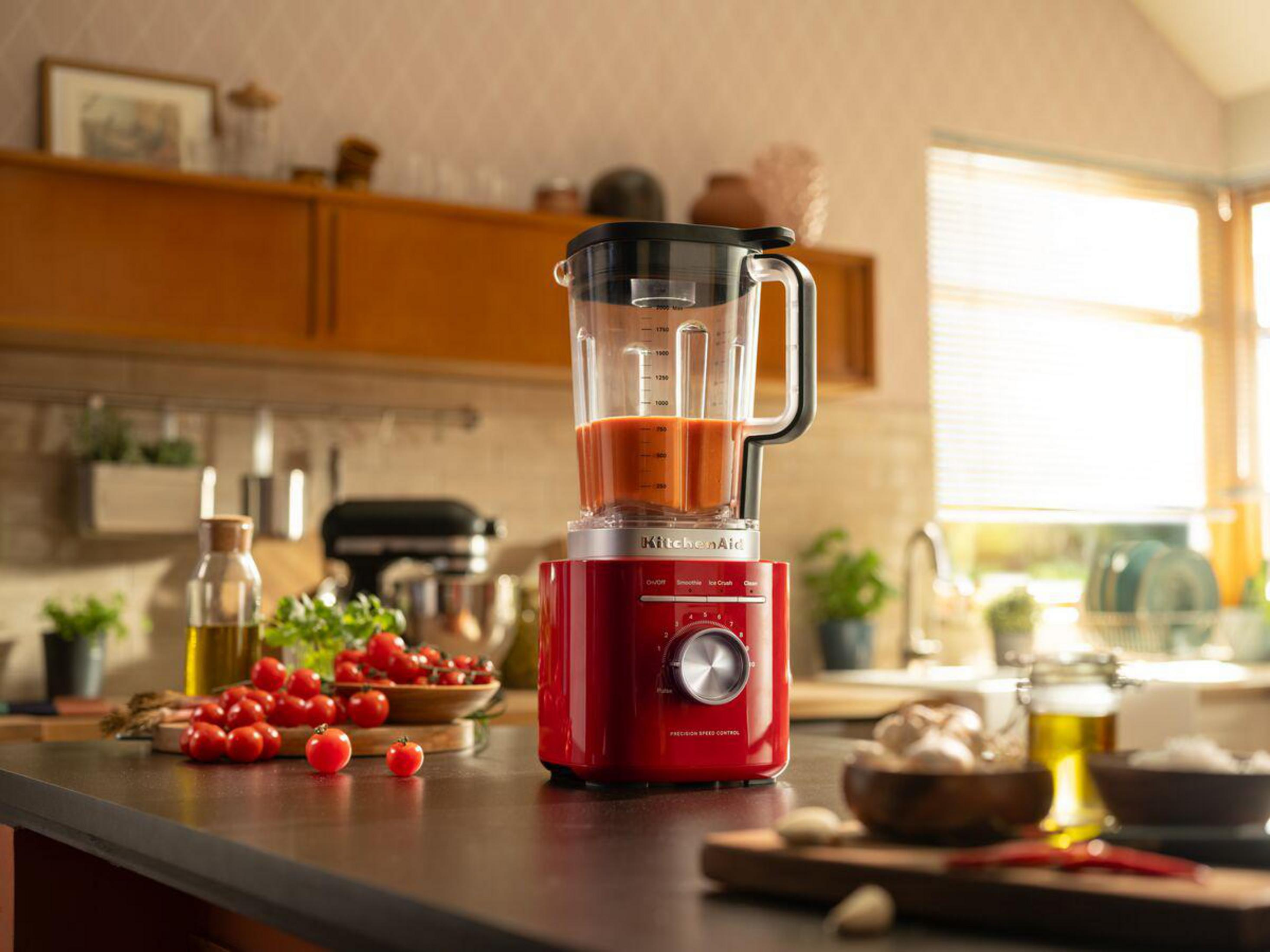 Rode blender met tomaten, olijfolie en knoflook in een keuken.