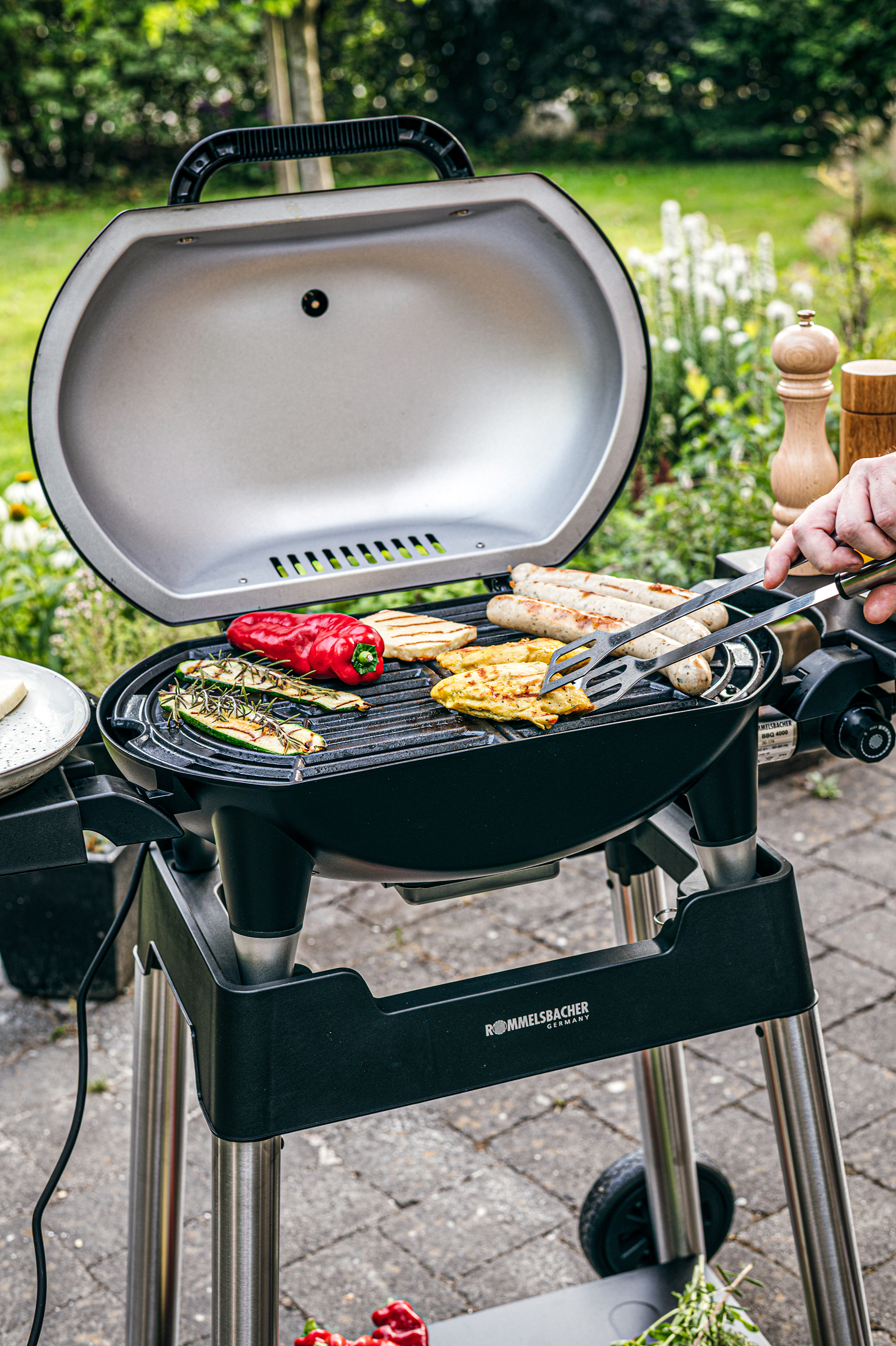 Ein Grill mit Bratwurst, Hähnchen, Paprika und Zucchini wird im Freien zubereitet.