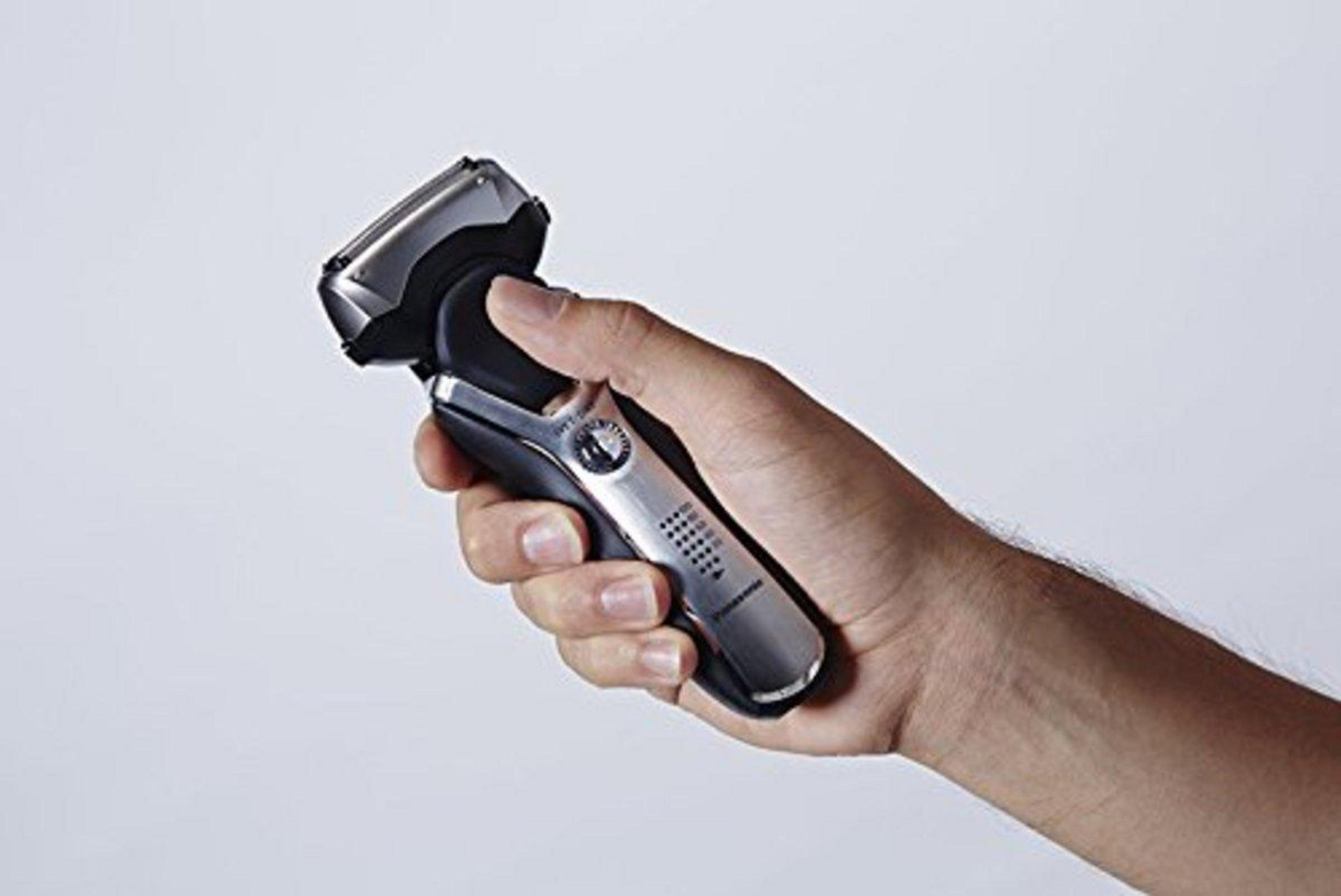Una mano tiene un rasoio elettrico argento e nero su sfondo bianco.