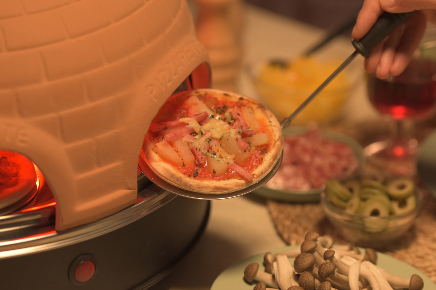 Een mini pizza wordt uit een oven gehaald. Belegd met ananas en ham.