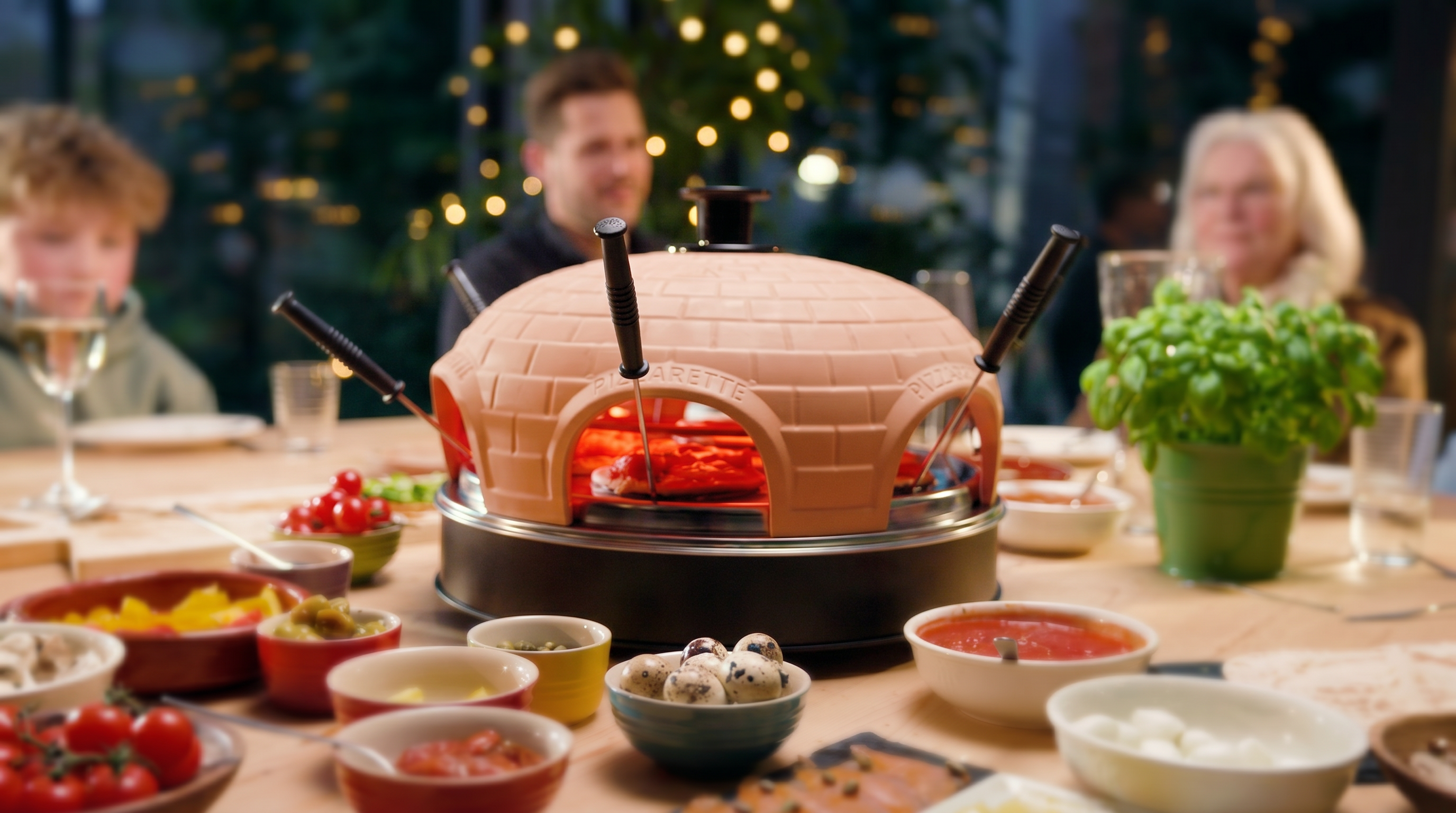 Een gezin eet aan tafel met een pizzarette en veel bijgerechten.