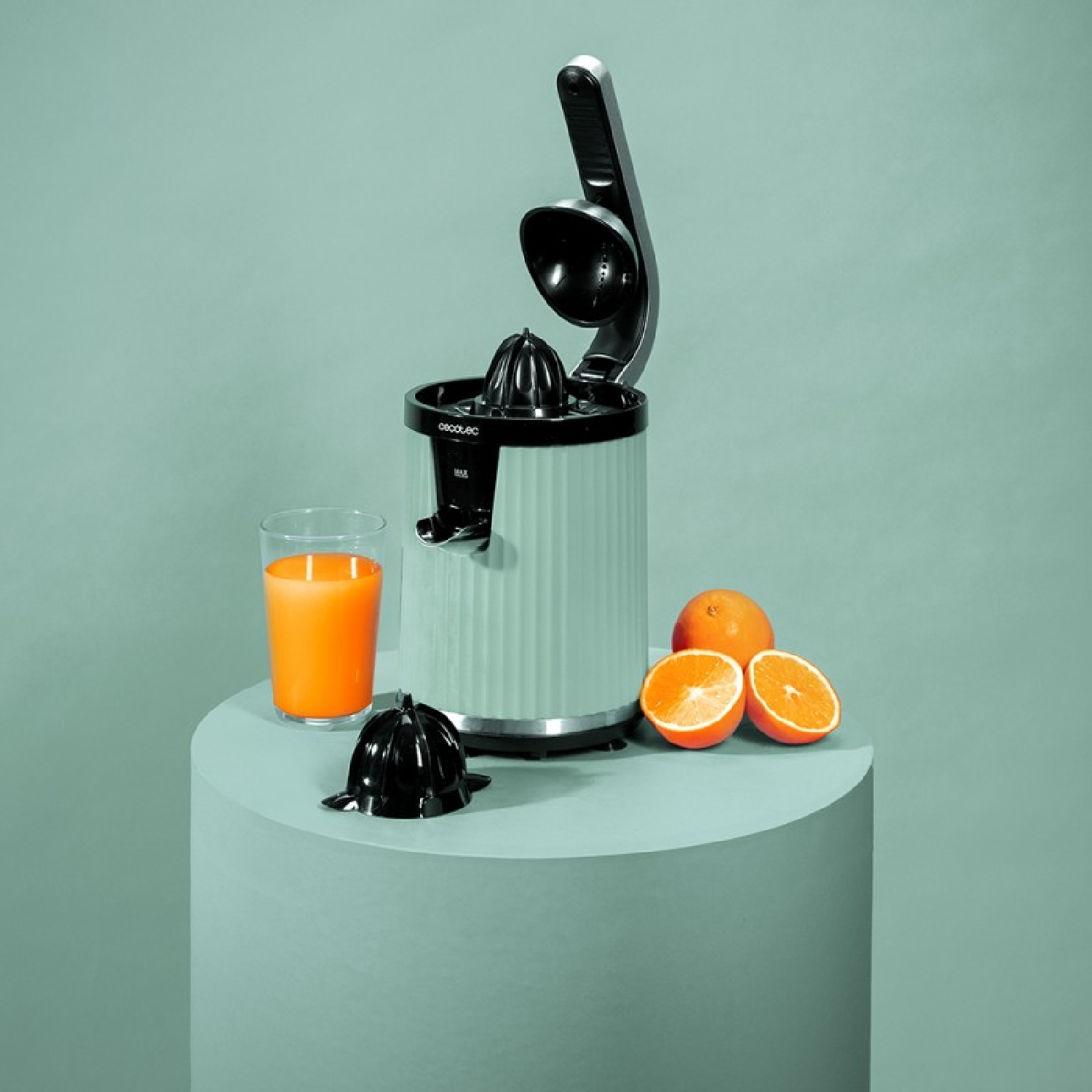 Licuadora verde claro con vaso de jugo de naranja, naranjas y tapa negra.