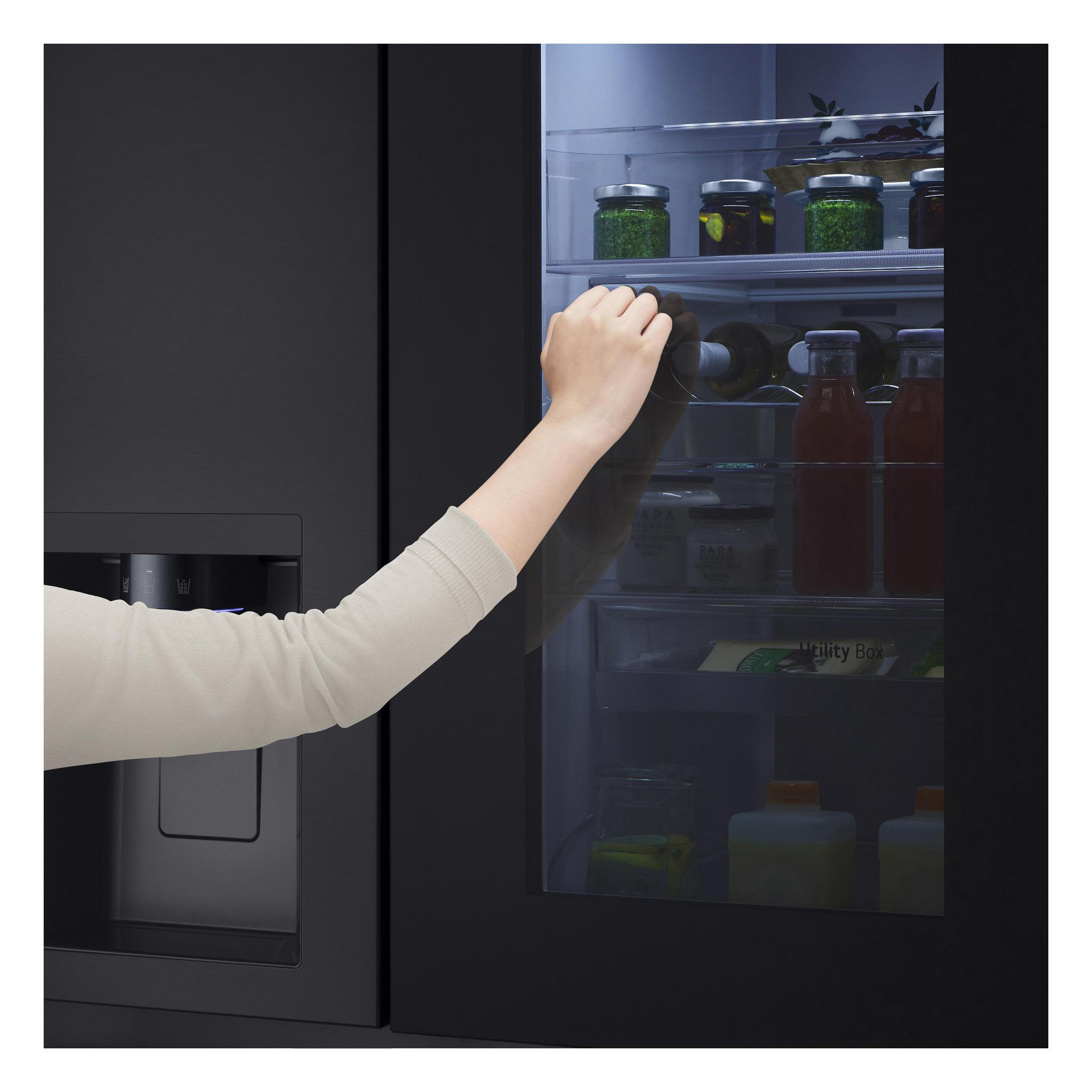 Eine Hand greift nach einer Flasche in einem schwarzen Kühlschrank mit Lebensmitteln.