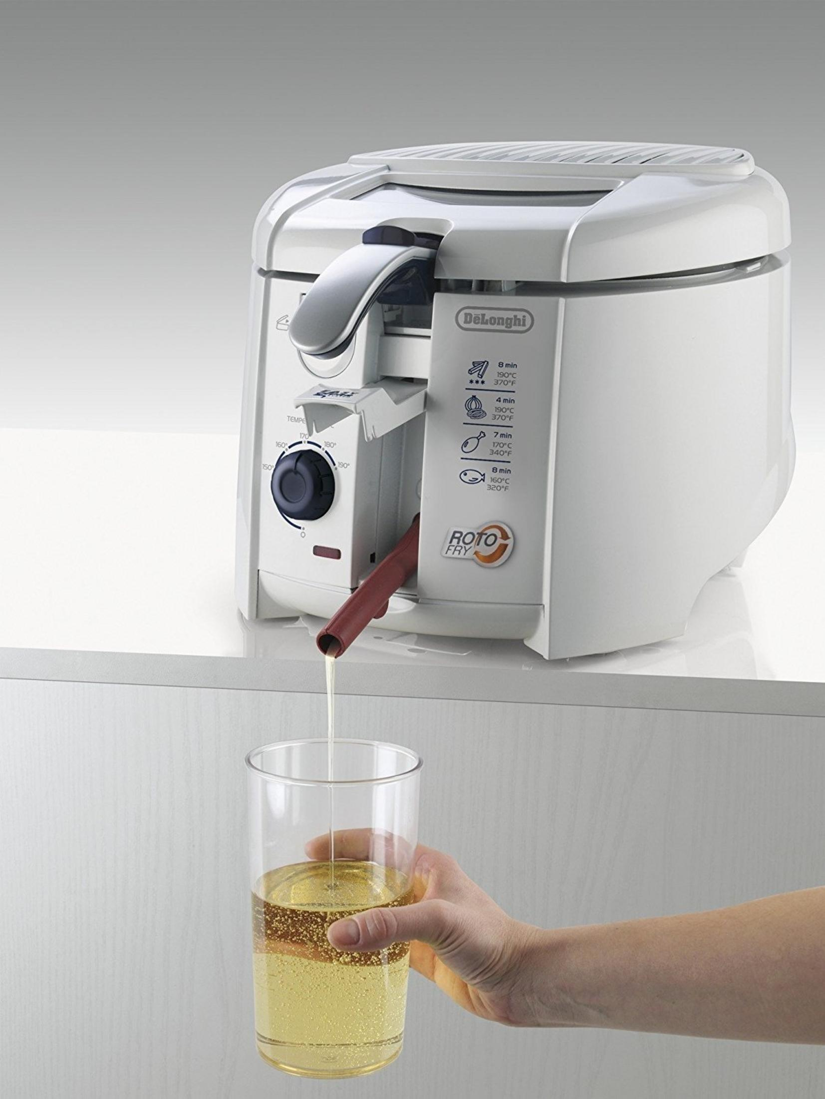 Eine weiße DeLonghi Roto Fry Fritteuse leert Öl in ein Glas, das von einer Hand gehalten wird.
