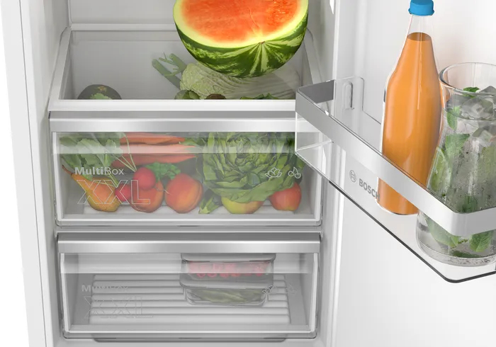 Een koelkast met fruit en groenten in lades en een fles sap.