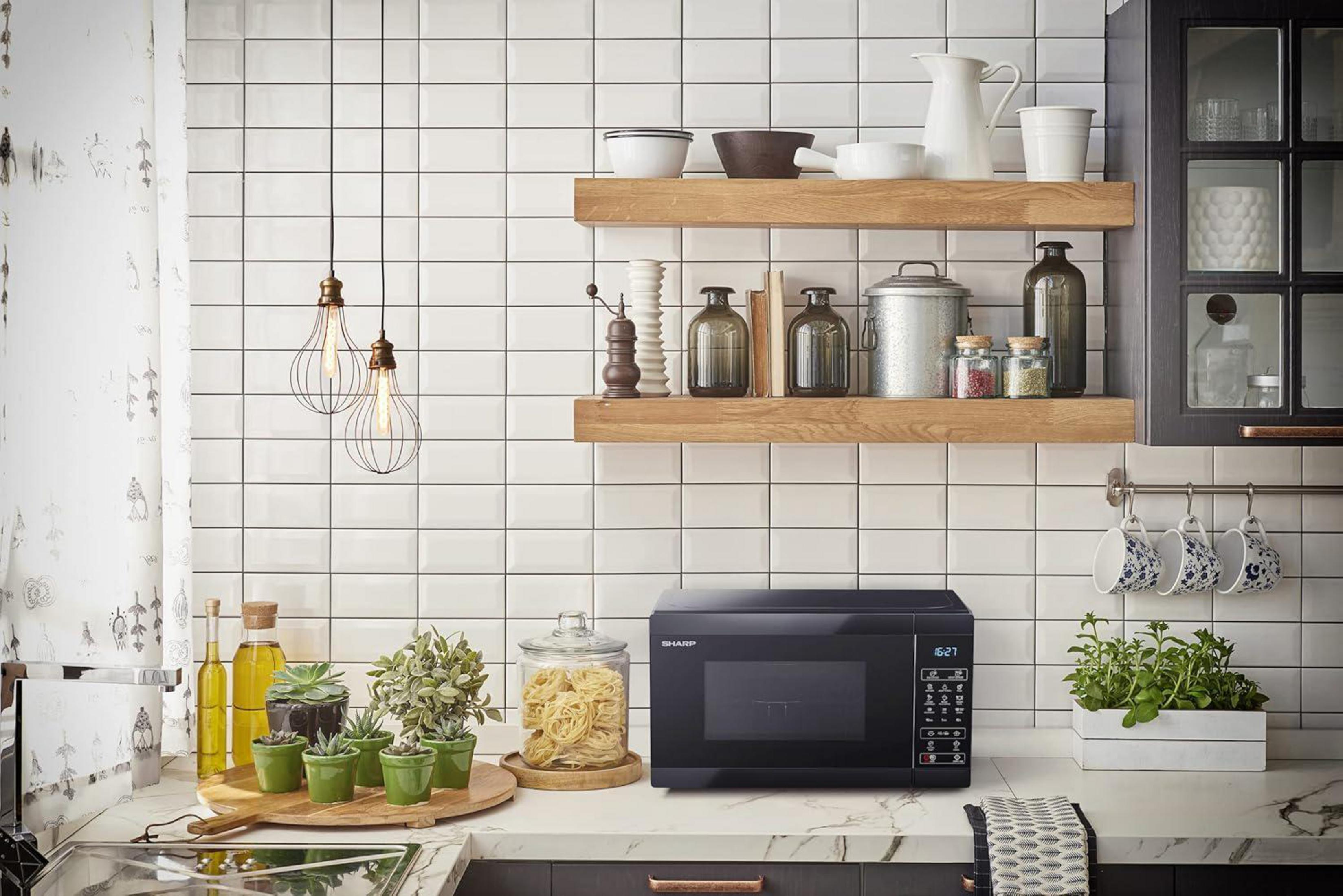 Cocina moderna con microondas negro, hierbas y vajilla en estantes colgantes.