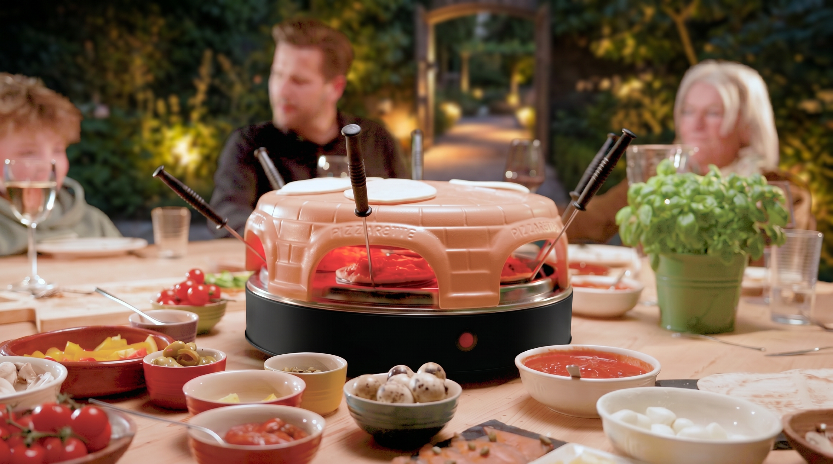 Familie geniet van buitenpizza met Pizzarette oven en toppings.