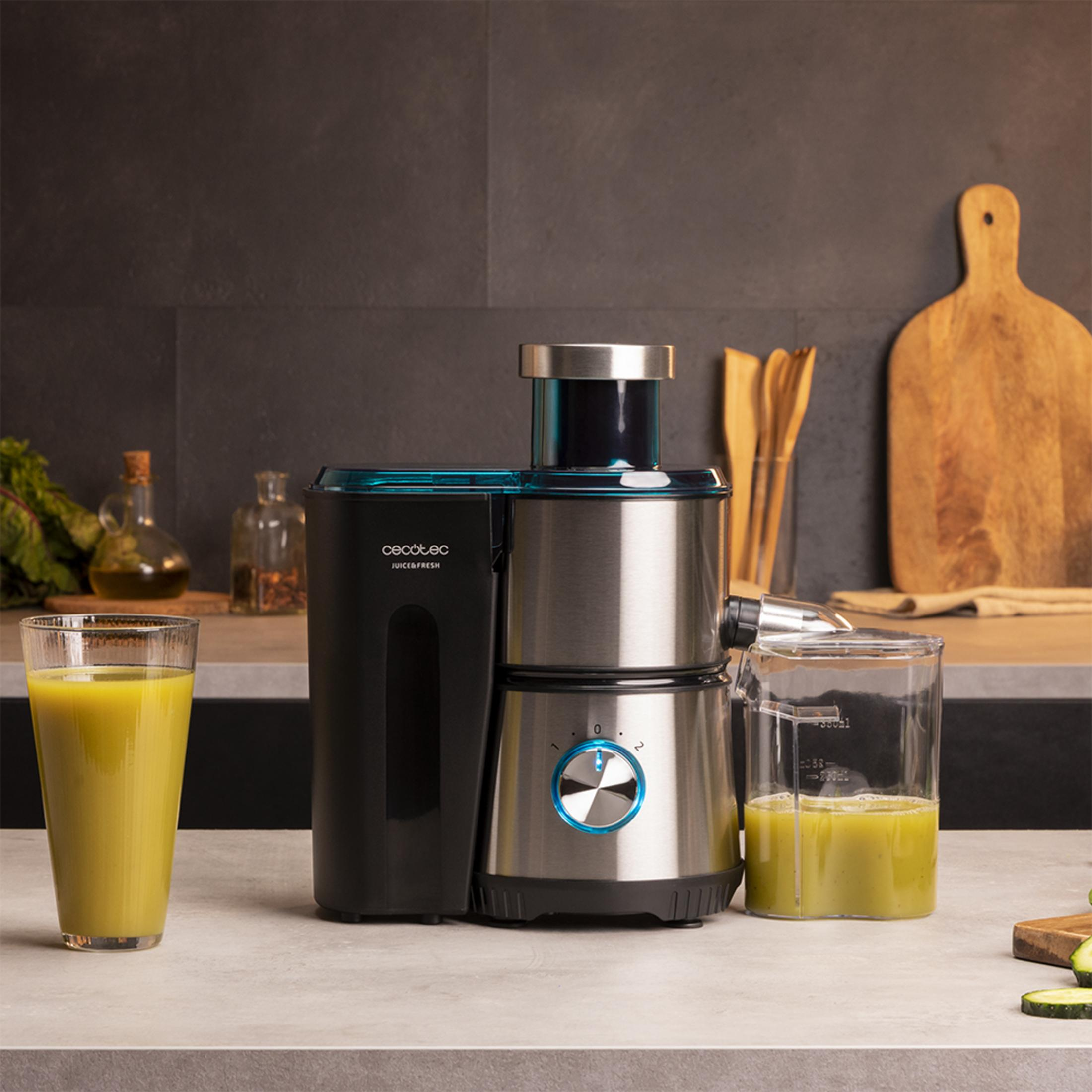 Un extractor de jugos está sobre una encimera con dos vasos de jugo al lado.