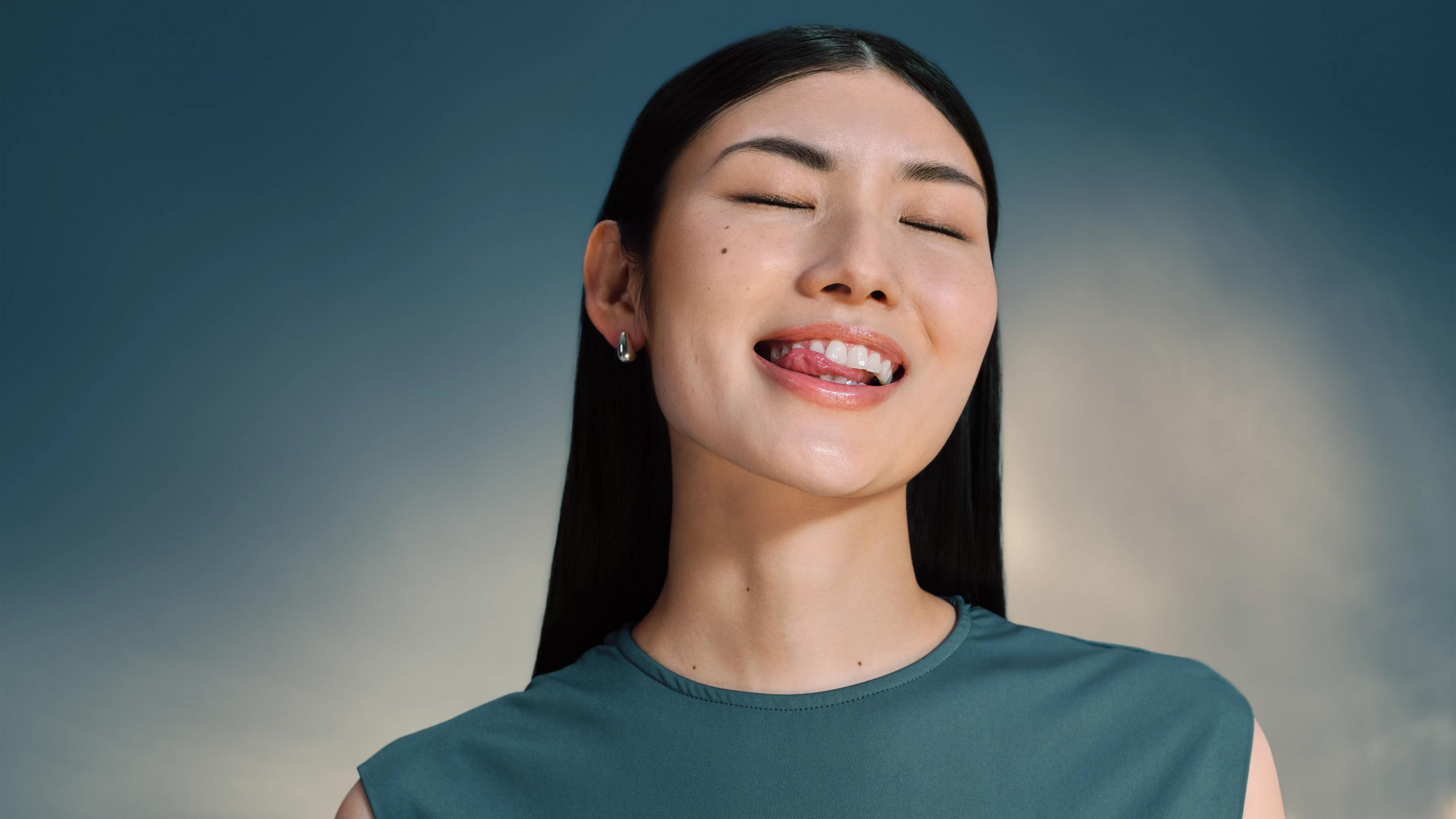 Mujer con los ojos cerrados se lame los labios, vistiendo un top verde.