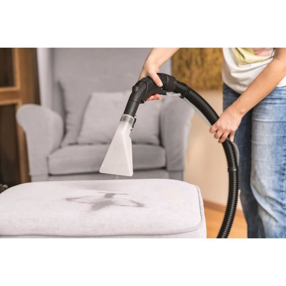 Una persona limpia un puf gris claro con una aspiradora de líquidos y sólidos.