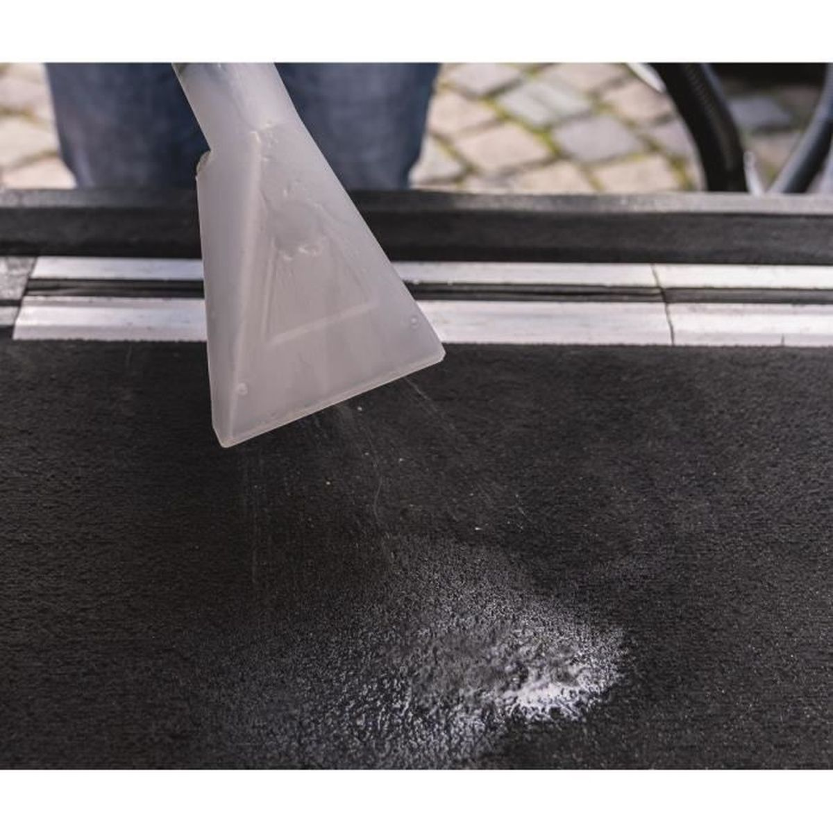 Una herramienta de tapicería de plástico transparente rocía agua sobre una alfombra oscura.