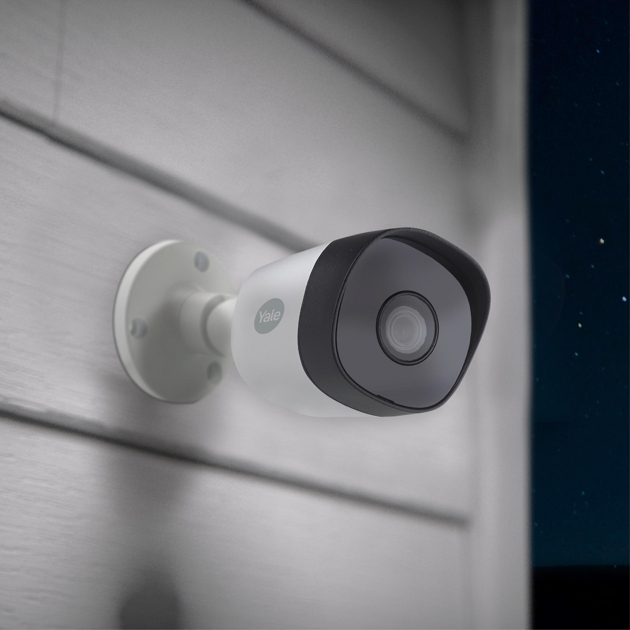 Una telecamera di sicurezza Yale bianca è montata su una parete di legno grigia.