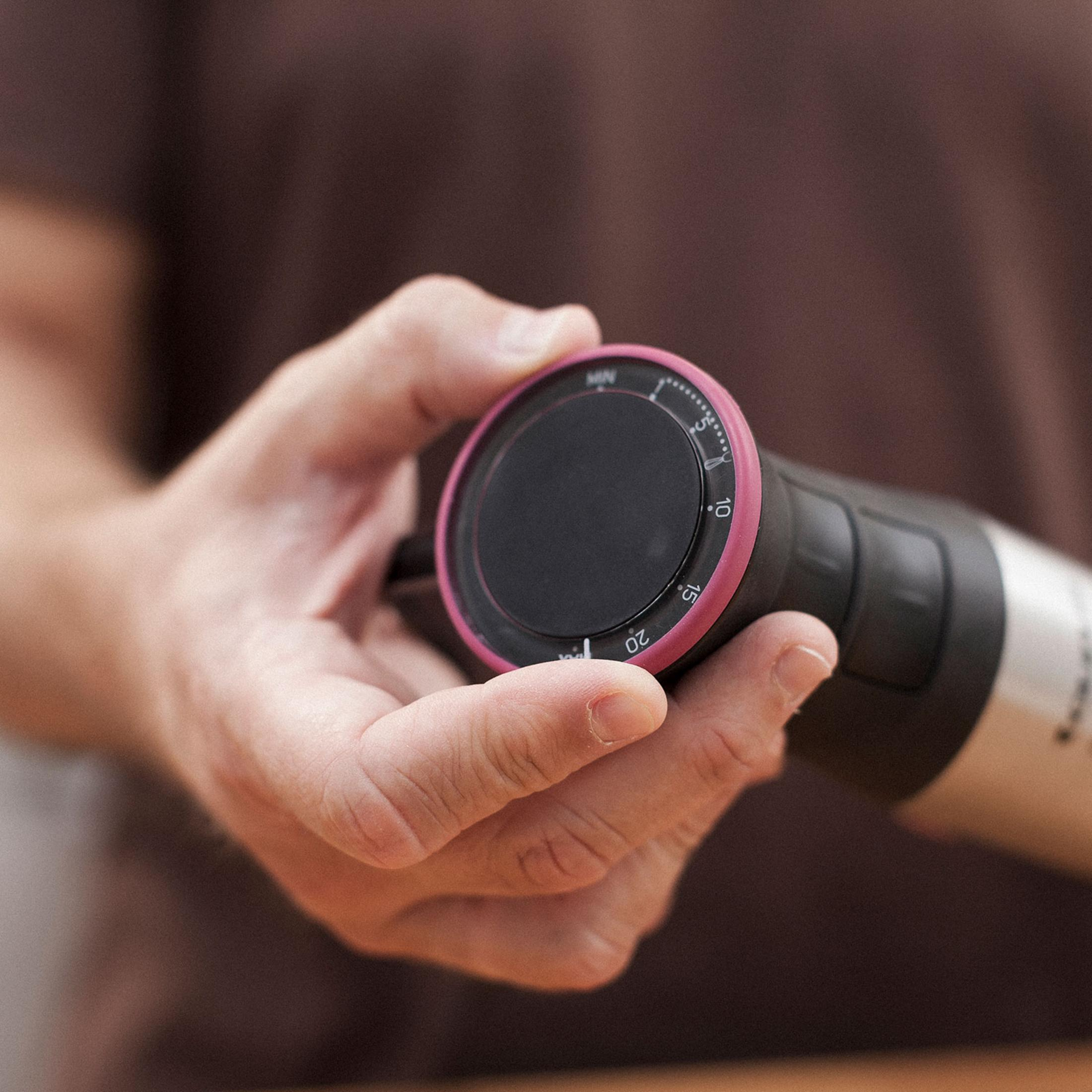 Una mano gira un dial negro con borde rosa y números.
