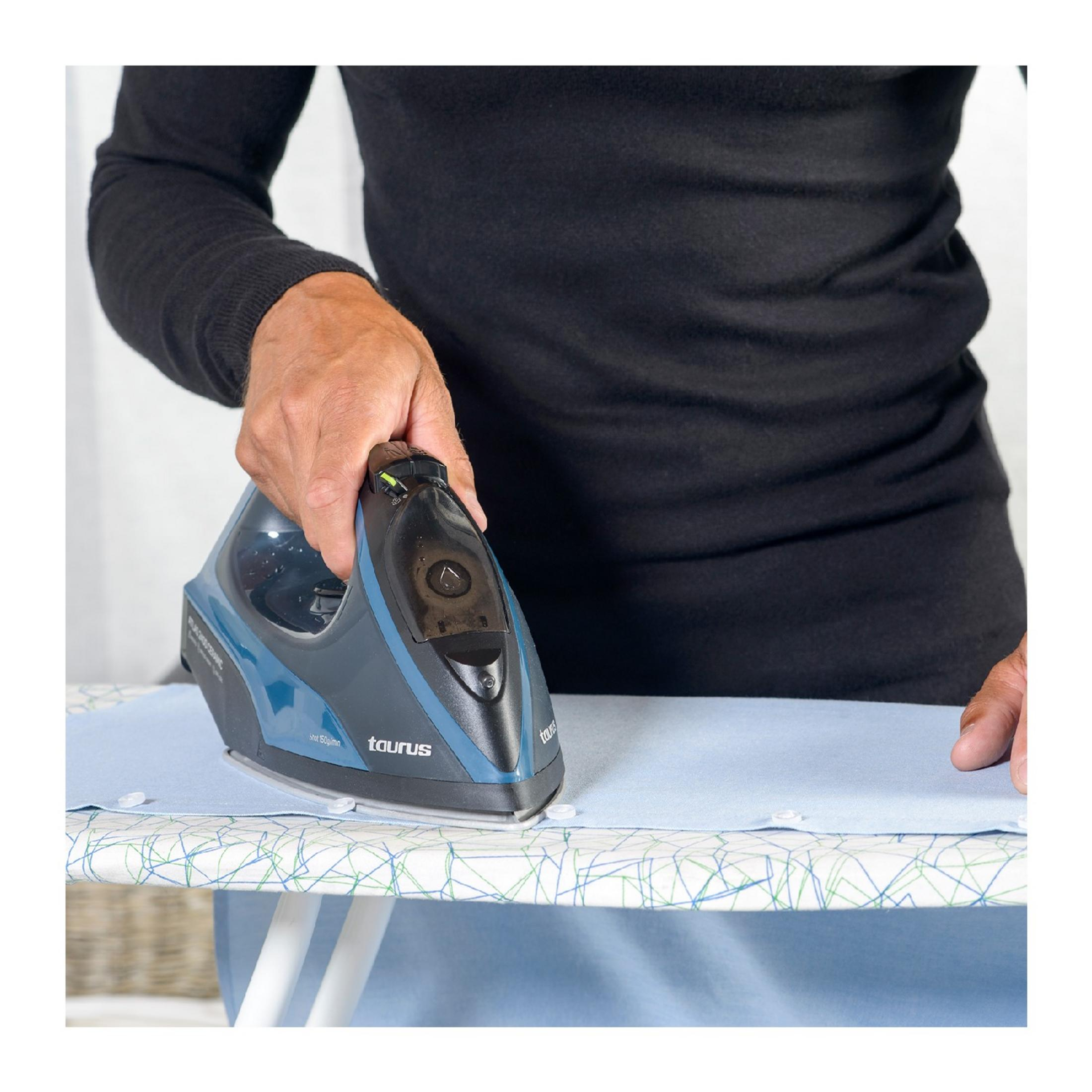 Una persona plancha una camisa azul sobre una tabla de planchar con una plancha azul.