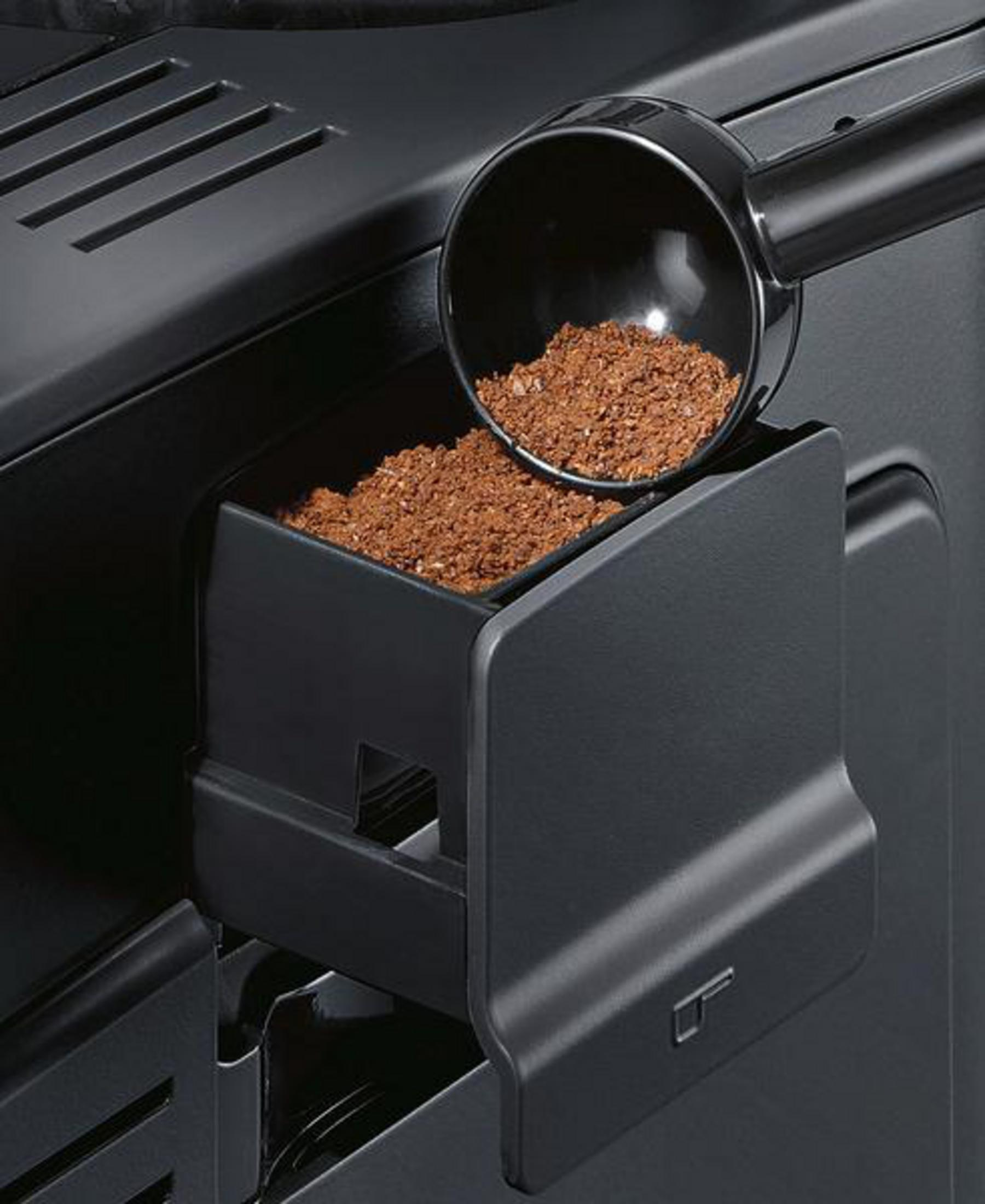Un misurino per caffè con caffè macinato sopra un vano su una macchina da caffè nera.
