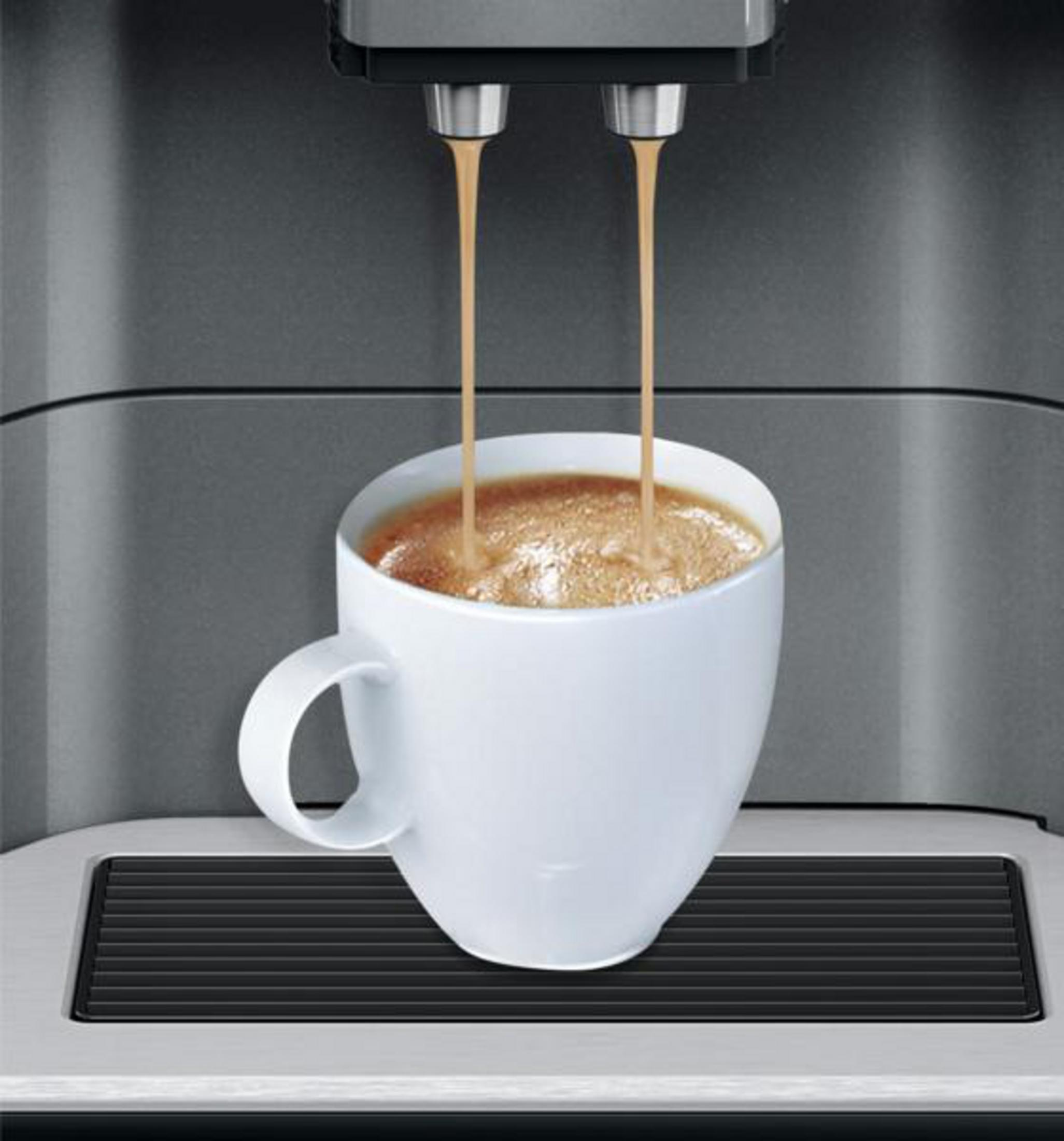 Due flussi di caffè scorrono in una tazza bianca da una macchina da caffè.