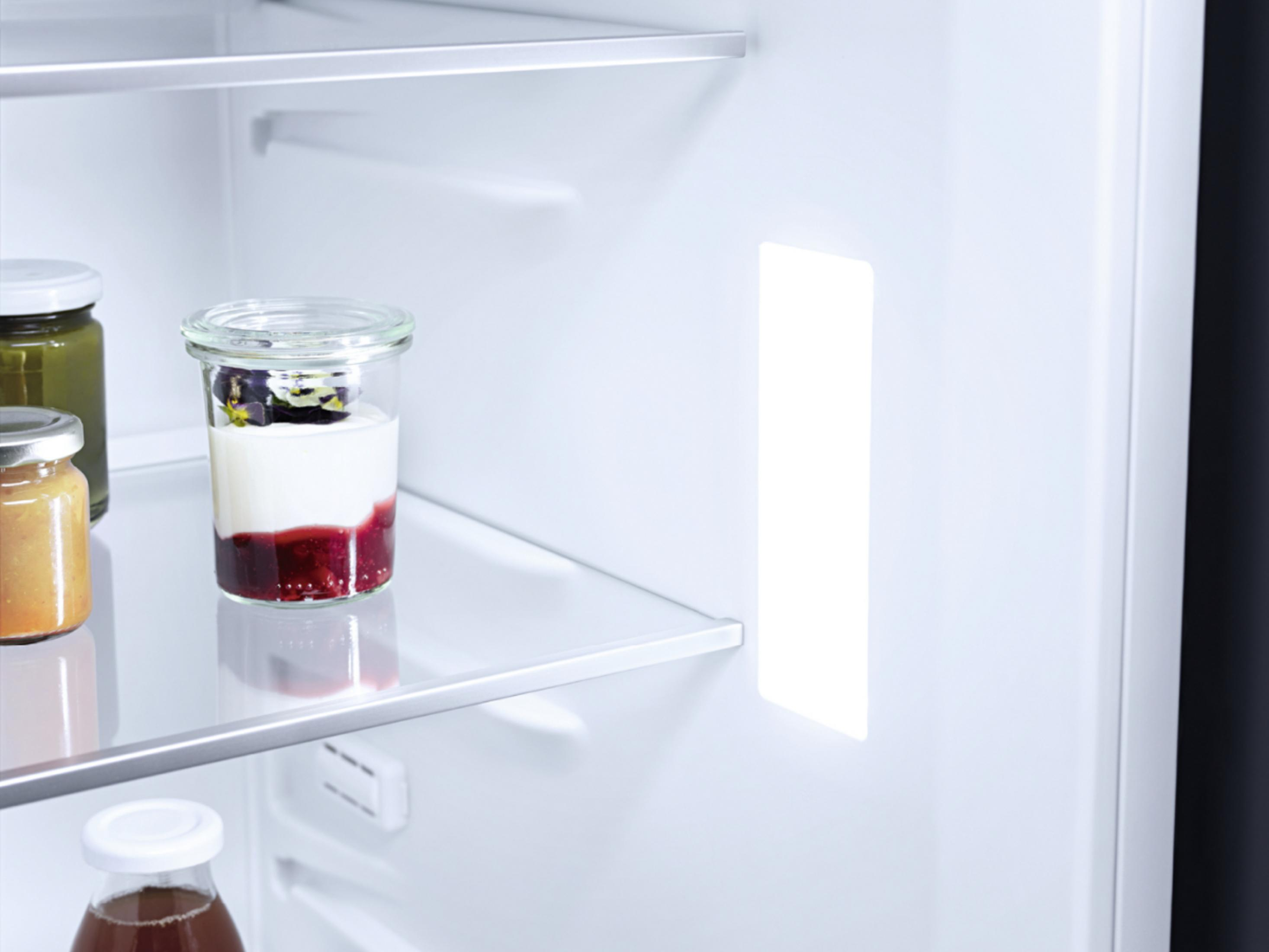 Ein offener Kühlschrank mit Gläsern mit Lebensmitteln und einer hellen LED-Beleuchtung.