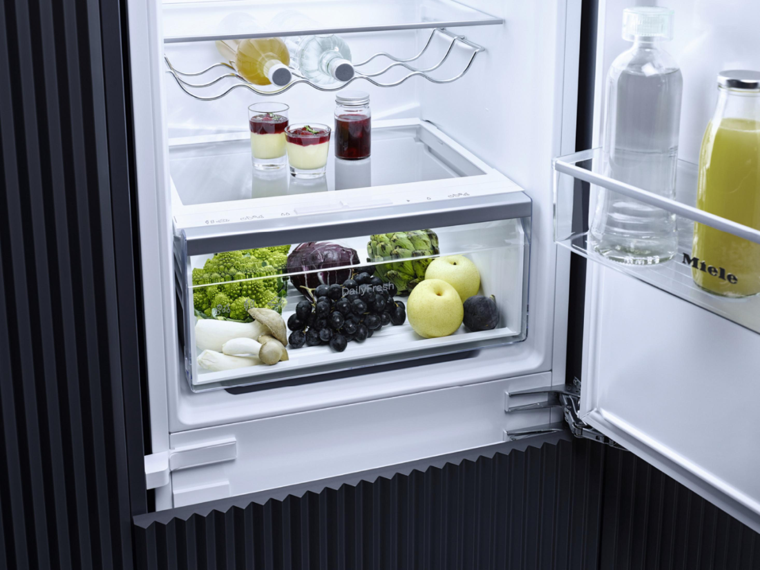 Ein offener Kühlschrank mit Lebensmitteln: Flaschen, Gläser und Obst im Fach.