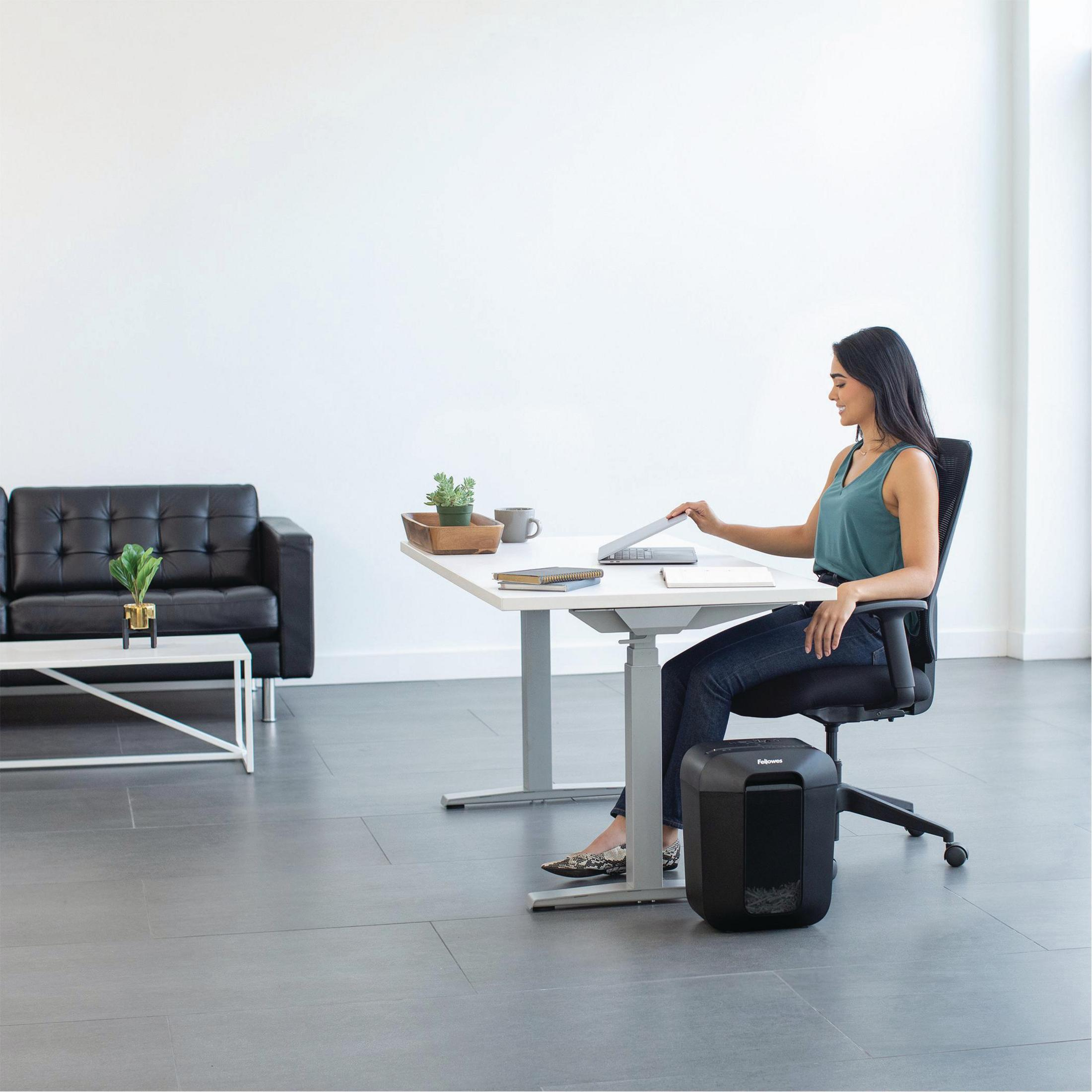 Femme au bureau ferme son ordinateur portable, déchiqueteuse à côté.
