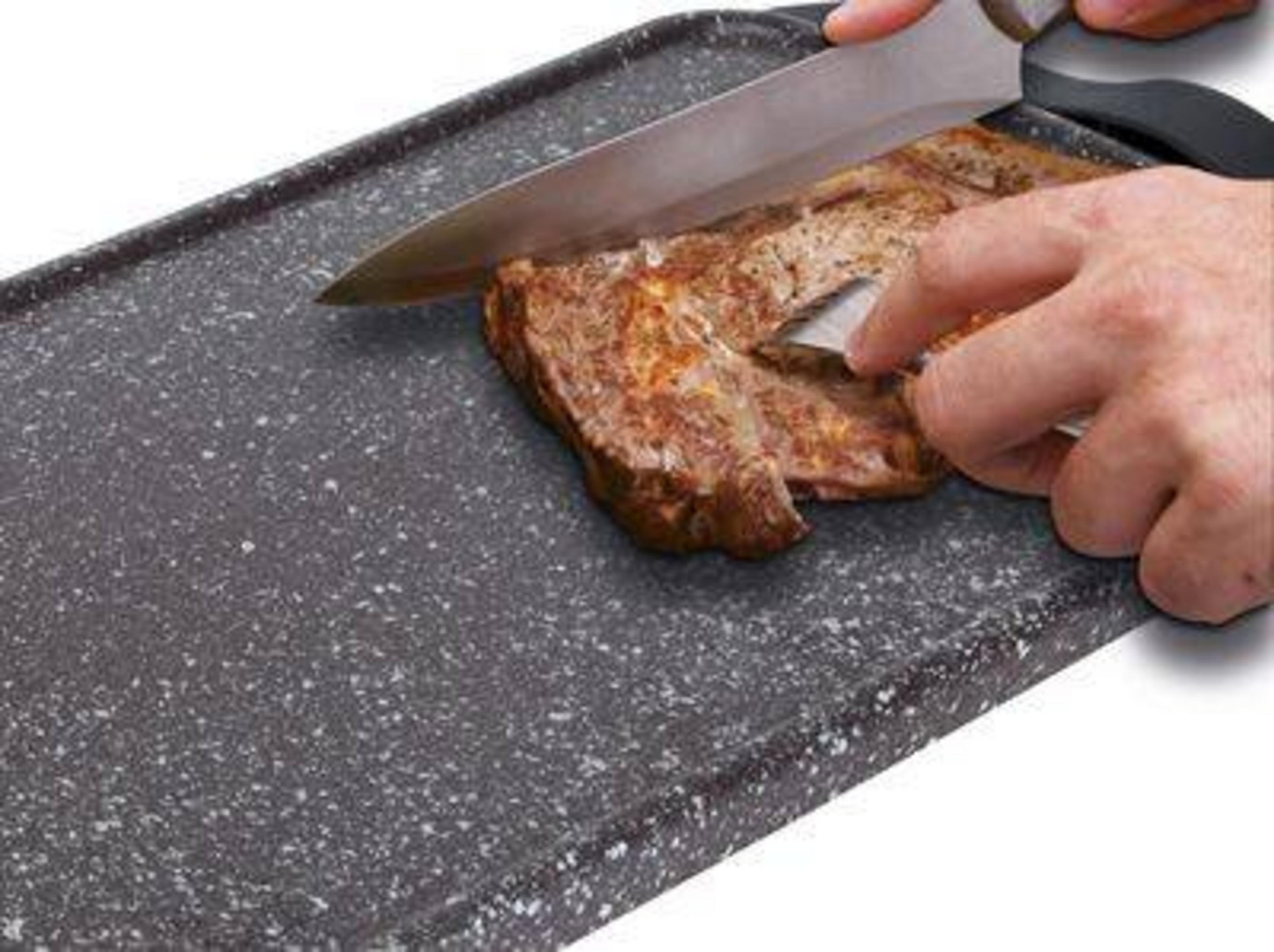 Un cuchillo corta un bistec cocido en una bandeja gris.