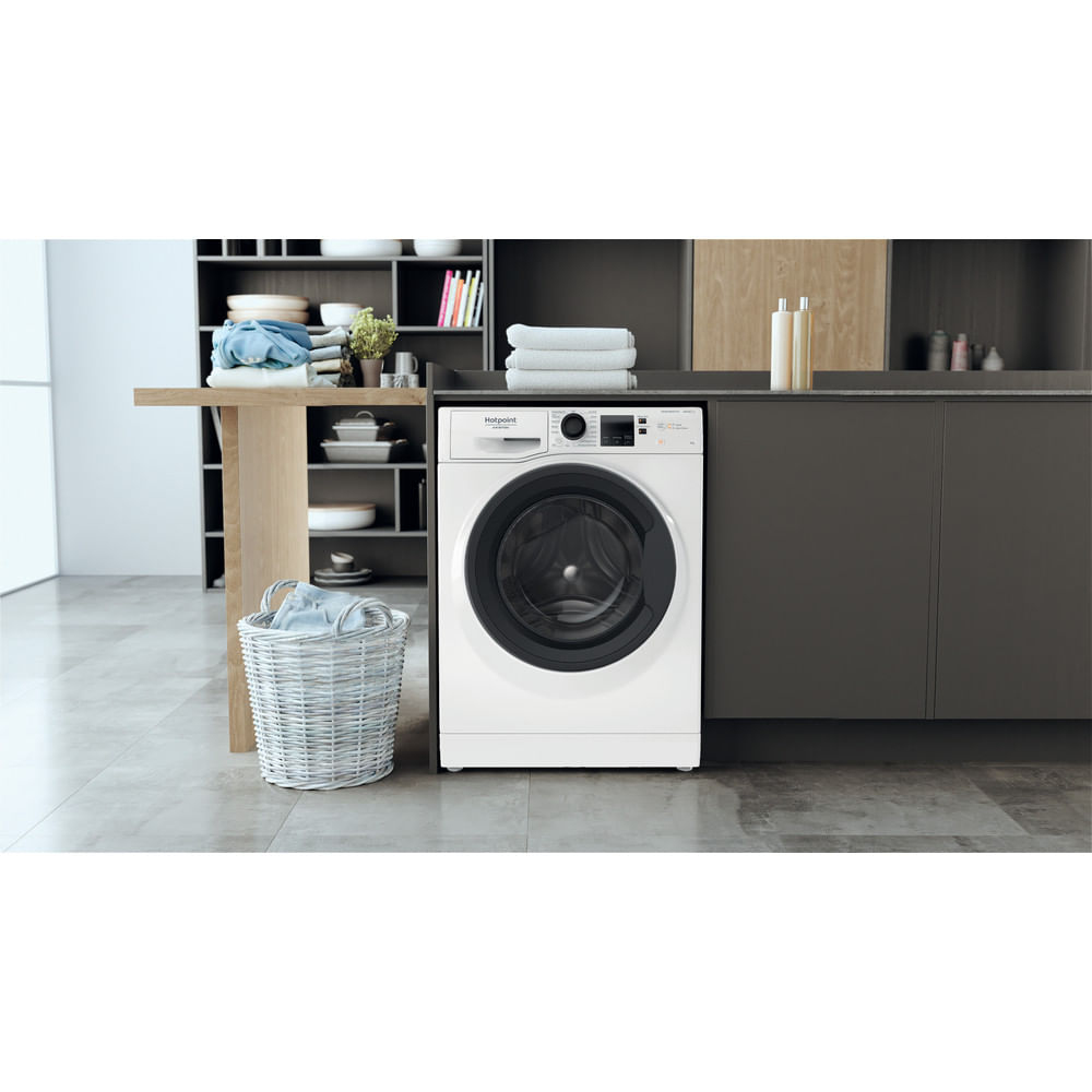 Una lavatrice Hotpoint bianca in una lavanderia moderna con un cesto della biancheria.