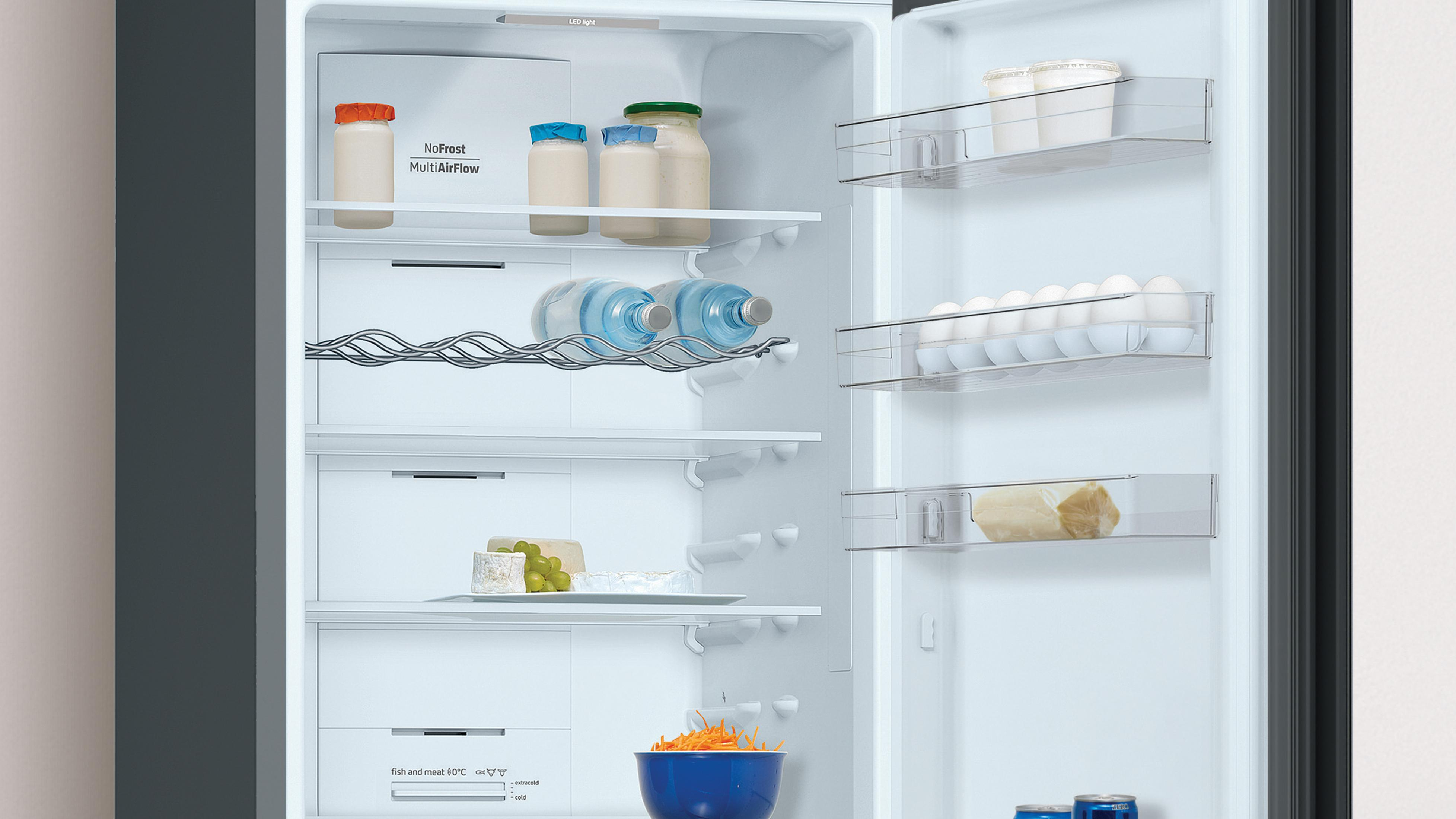 Un refrigerador abierto con botellas, huevos, queso y zanahorias.